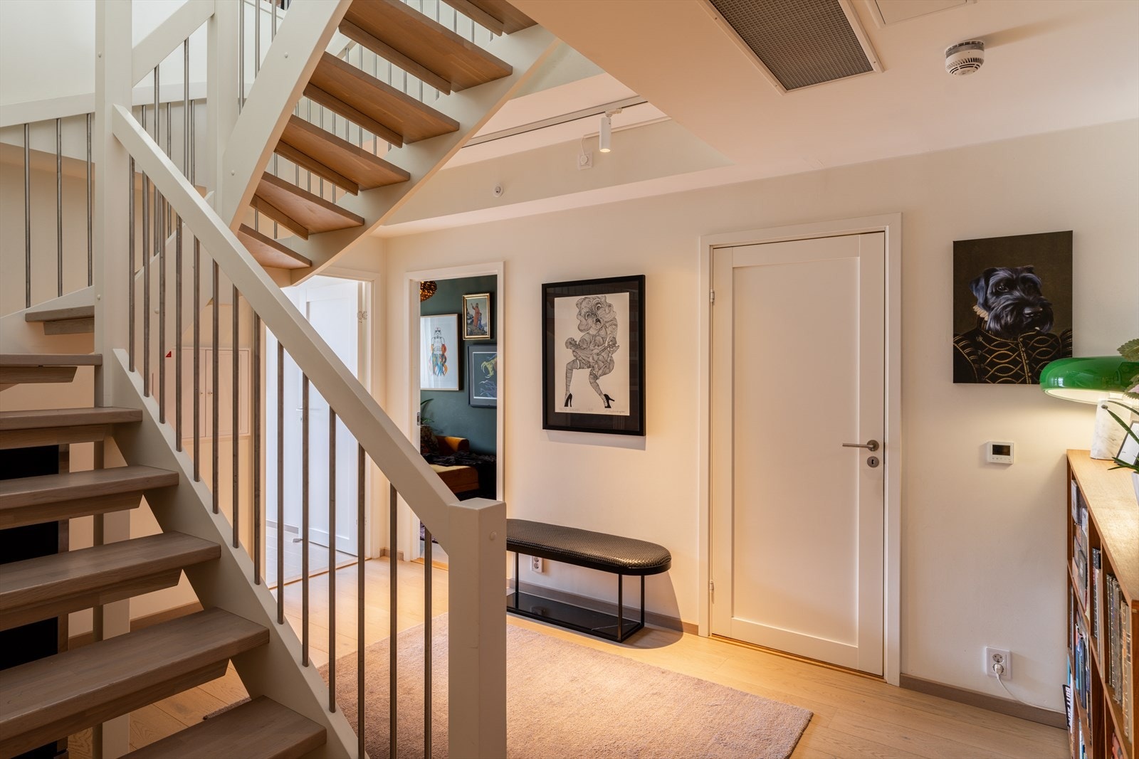 Romslig hall med gode muligheter for både oppbevaring, oppbevaring under trapp og møblering med eksempelvis bokhyller eller annen innredning. Fra hallen er det adkomst til boligens to soverom samt til et lekkert baderom. Galleribilde