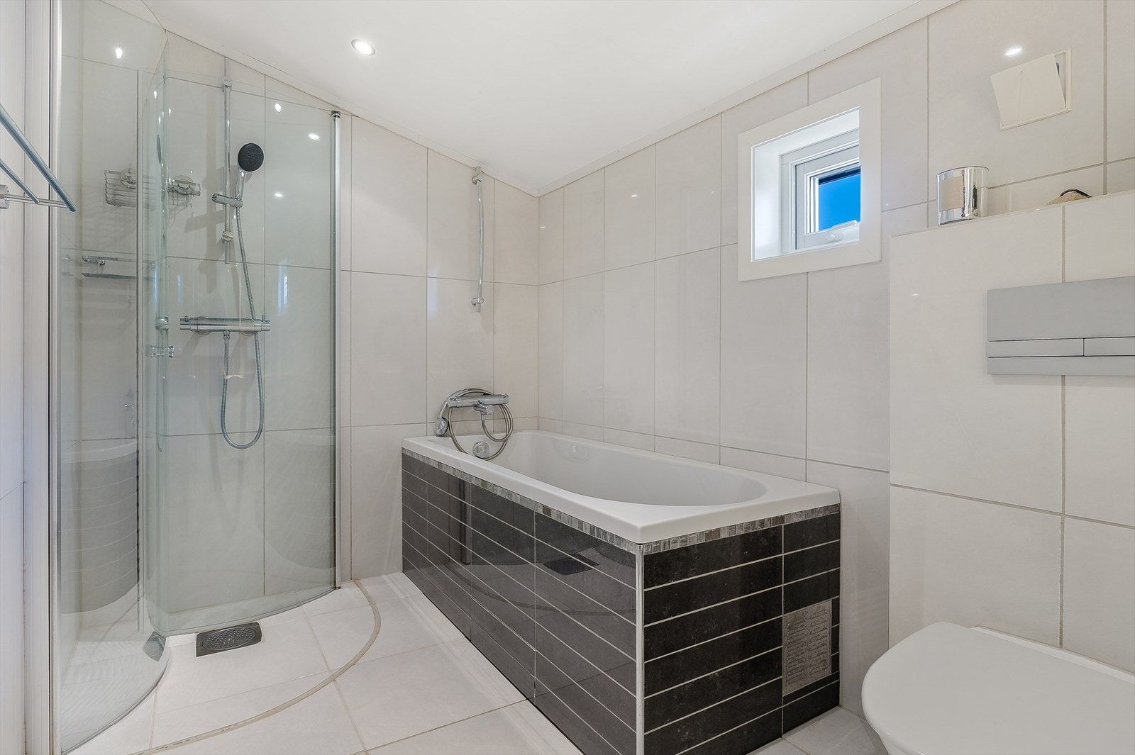 Badet er innredet med vegghengt wc, dusj med glassdør, spotlights i taket, badekar, servant og møblement. Galleribilde