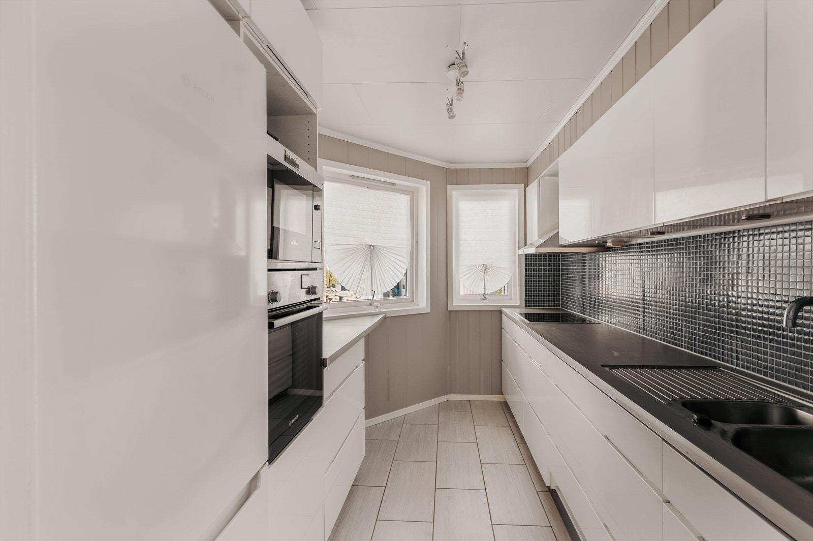 Boligens kjøkkeninnredning har hvite, slette fronter og laminat benkeplate. Galleribilde