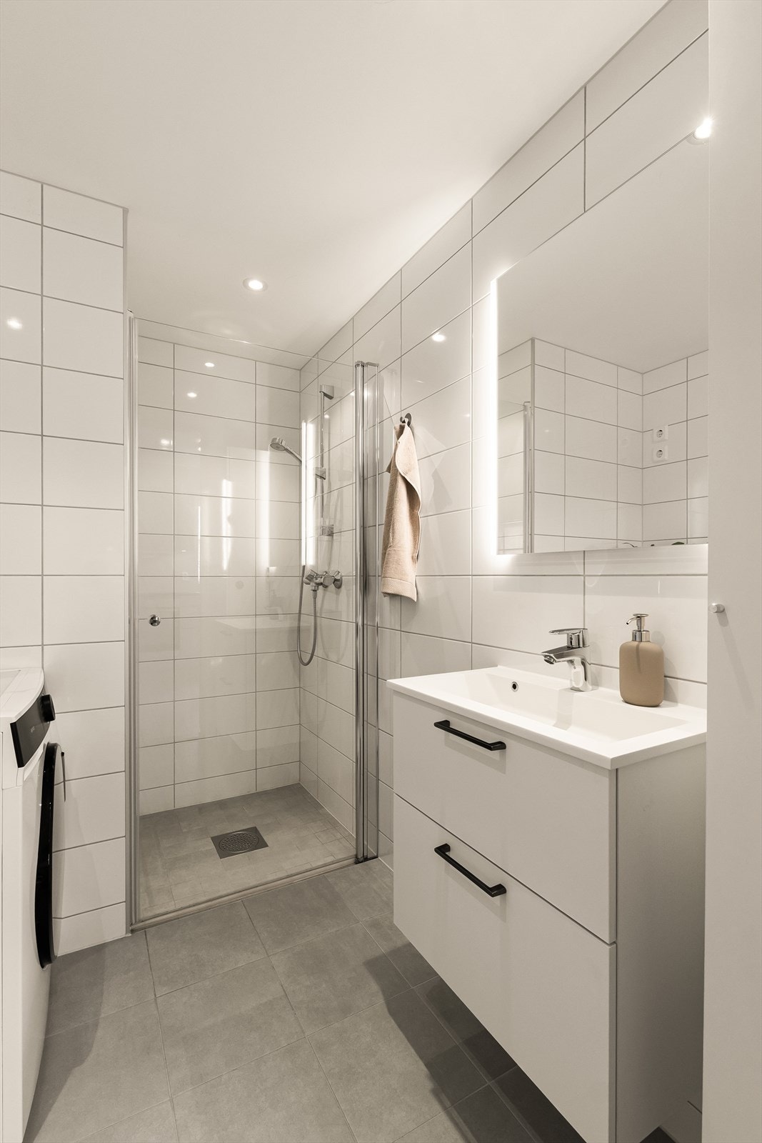 Badet er utstyrt med servant med tilhørende møblement, speil med belysning, vegghengt toalett samt dusjløsning med dusjdør. Galleribilde