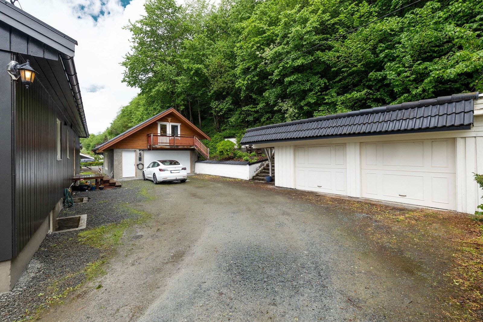 Romslig gårdsplass med gode parkeringsmuligheter. Eiendommen har dobbelt garasje, og romslig enkelt garasje med innredet loftsetasje. El-billader på garasjen foran bilen. Galleribilde