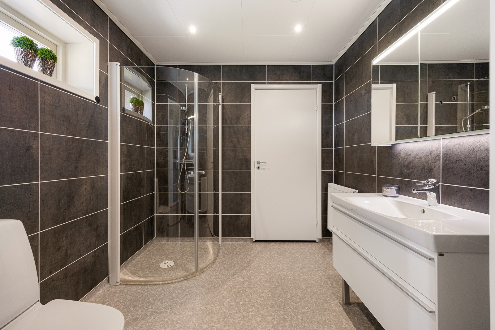 Videre finnes gulvmontert toalett og dusjhjørne med innsvingbare glassdører. I tilknytning til badet ligger en praktisk bod. Galleribilde