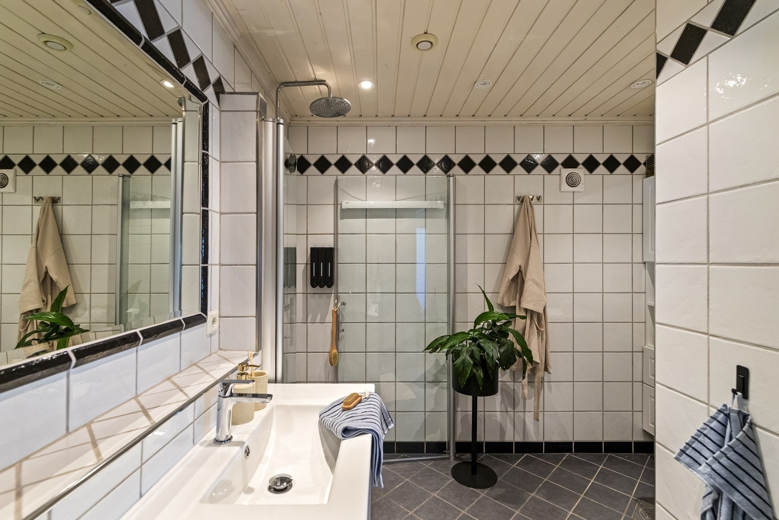 Badet inneholder et veggmontert toalett, dusjhjørne med en herlig regnfallsdusj, en hvit baderomsinnredning med nedfelt servant, samt praktisk opplegg for vaskemaskin under overskap. Galleribilde