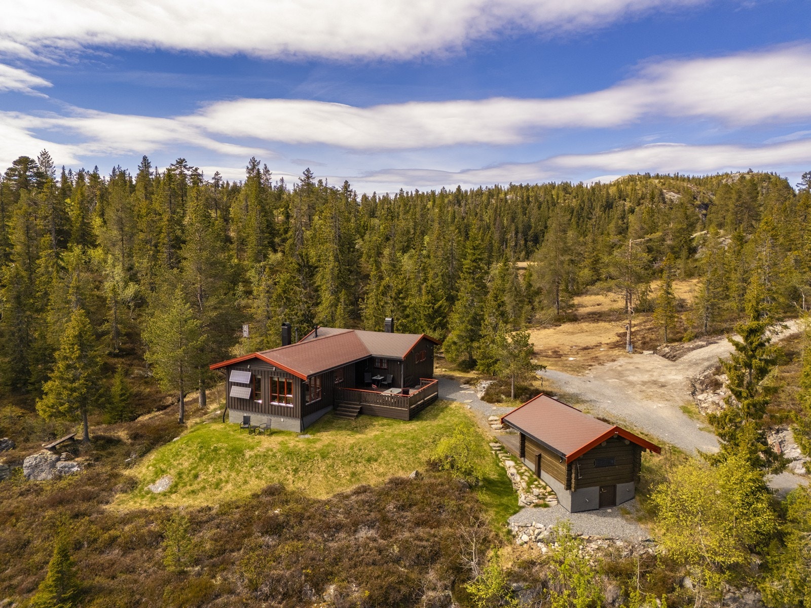 Oversikt over eiendommen med hovedhytte og uthus, omkranset av skog. Galleribilde