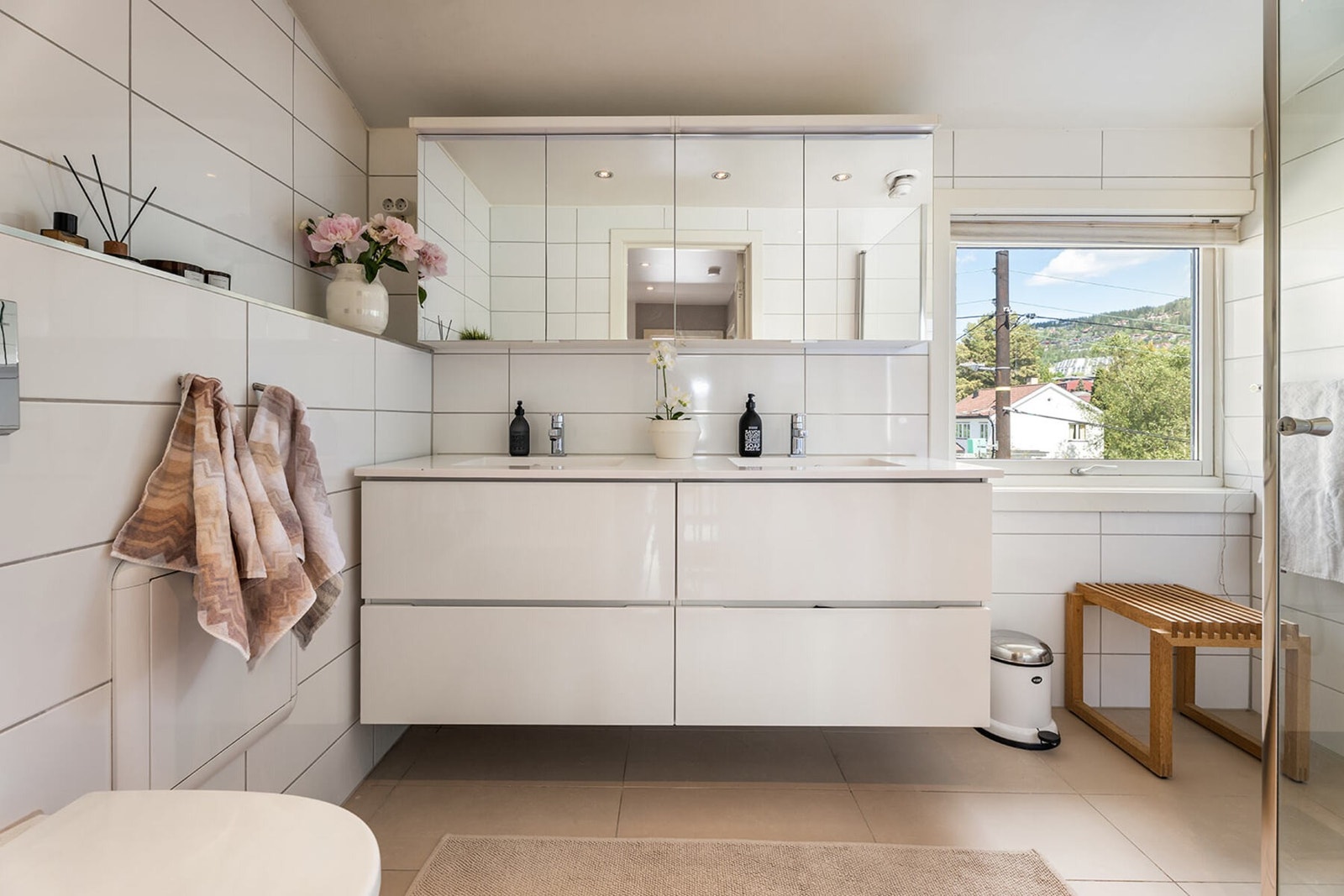 Badet er flislagt med hvite fliser og lyst gulv, og er innredet med dusjhjørne med glassdører. Galleribilde