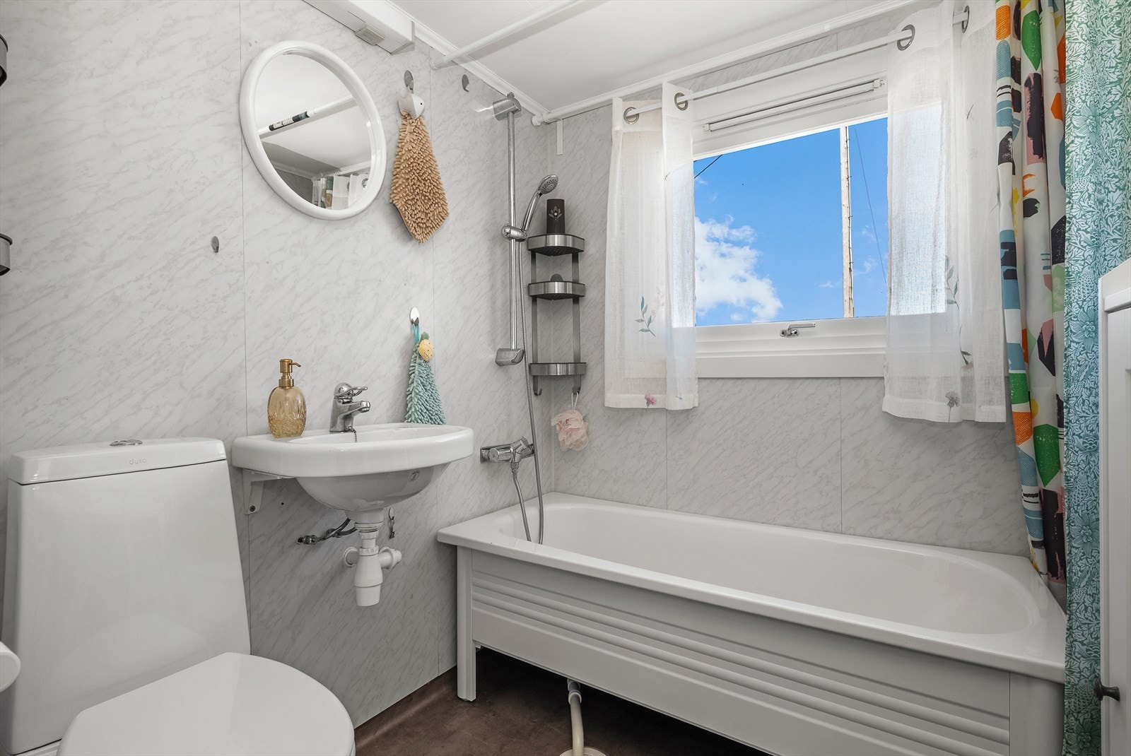 Lyst baderom utstyrt med toalett, servant og badekar. Galleribilde