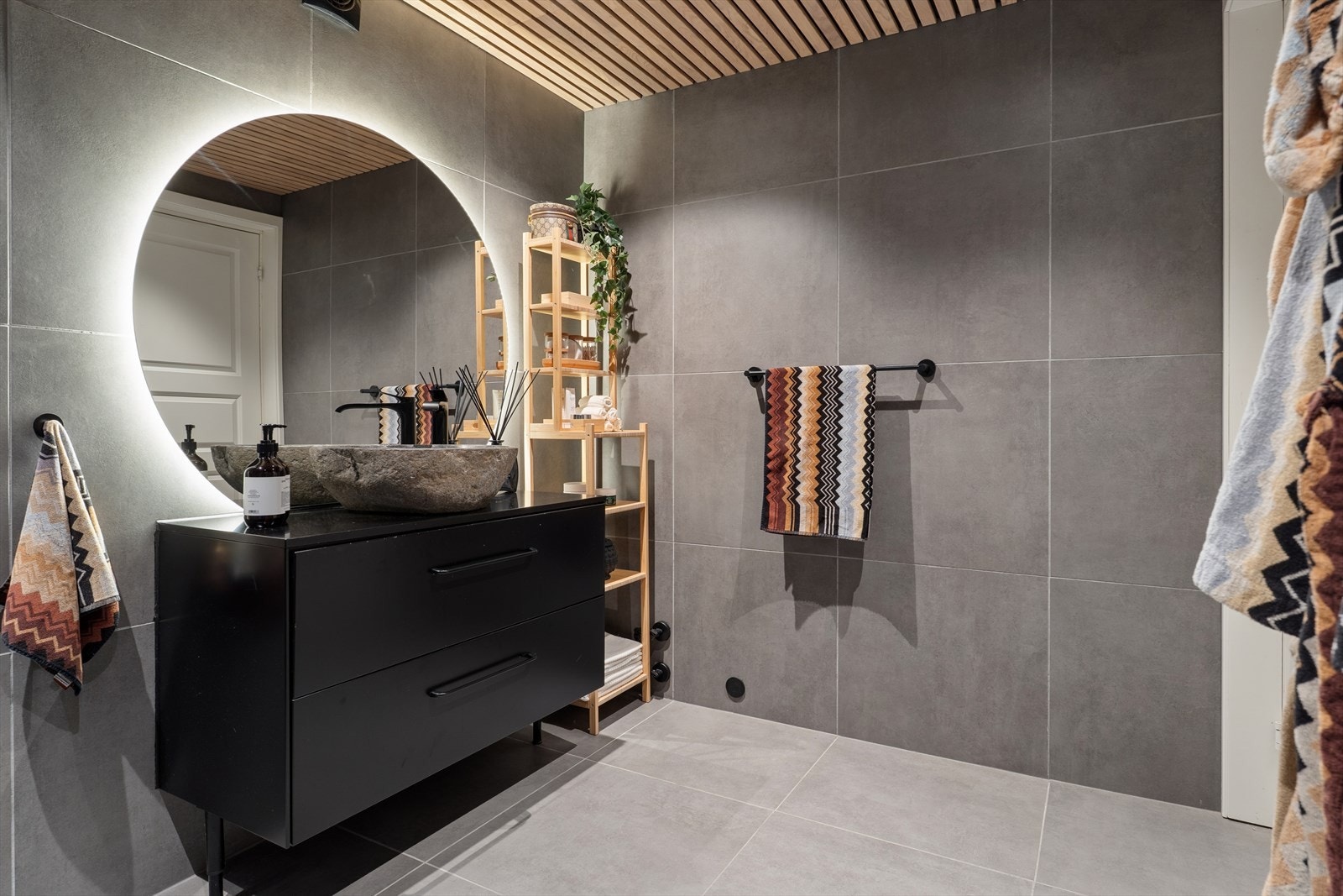 Badet er innredet med en moderne baderomsinnredning, speil med lys, veggmontert toalett og dusjhjørne med regndusj og hånddusj. Galleribilde