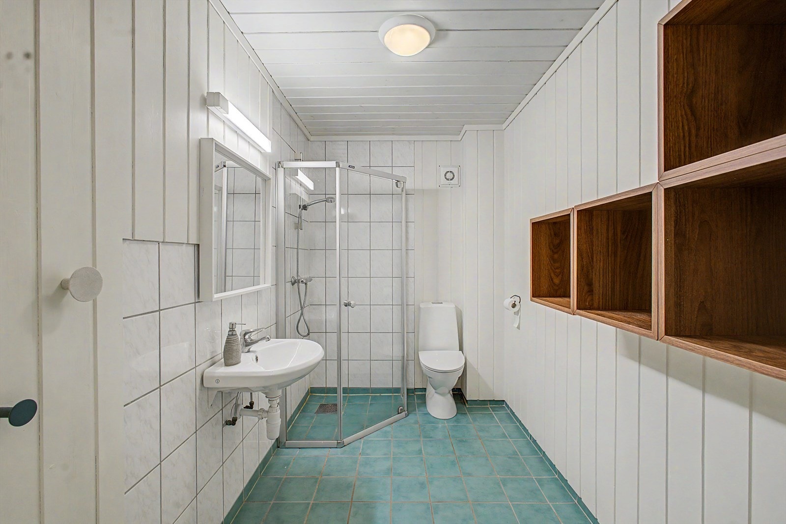Badet er utstyrt med dusjvegger, servant og toalett. Elektrisk styrt vifte sørger for ventilasjon. Galleribilde