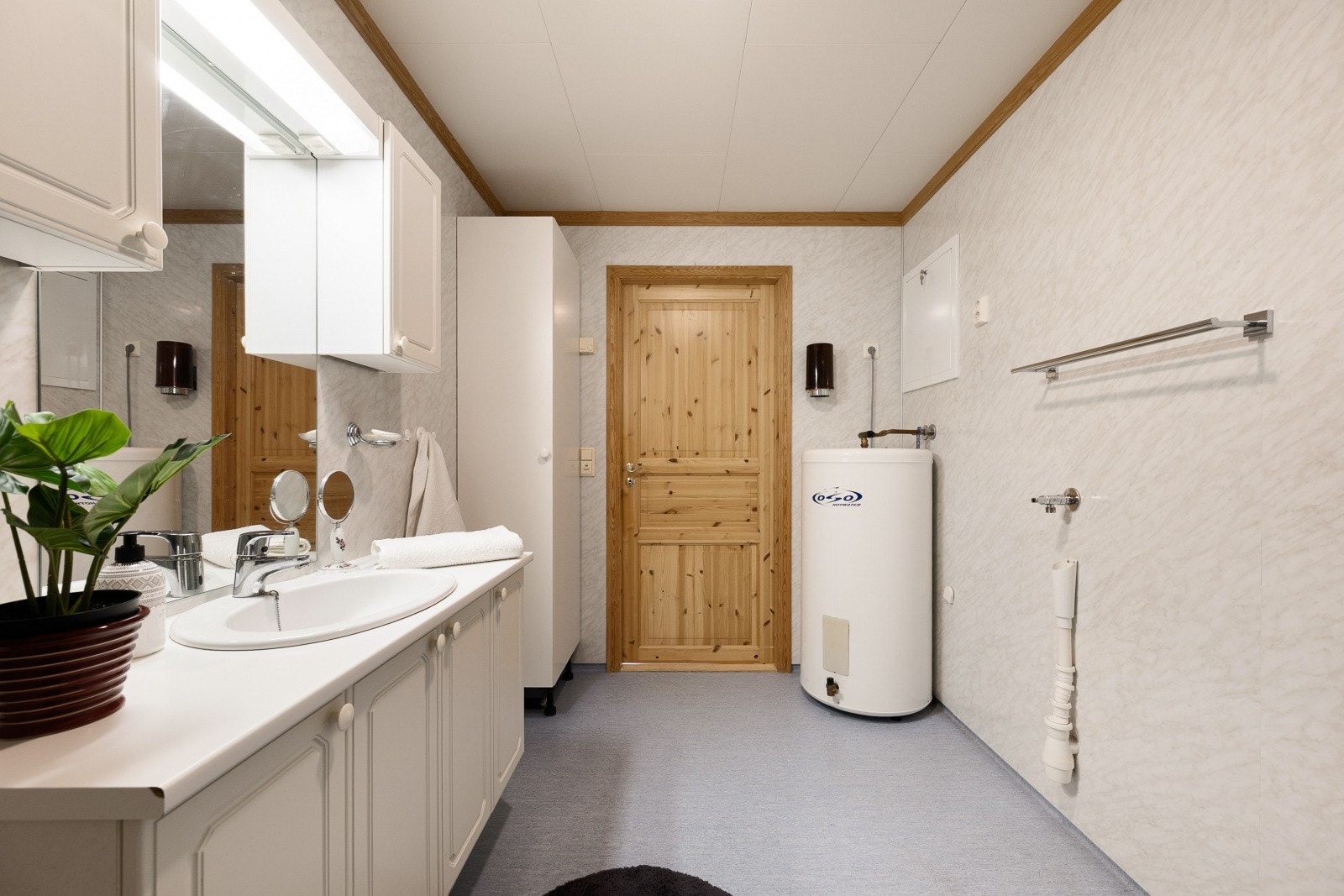 Badet er innredet med servant med underskap, speil med tilhørende belysning, dusjvegger, gulvmontert wc og opplegg for vaskemaskin. Galleribilde