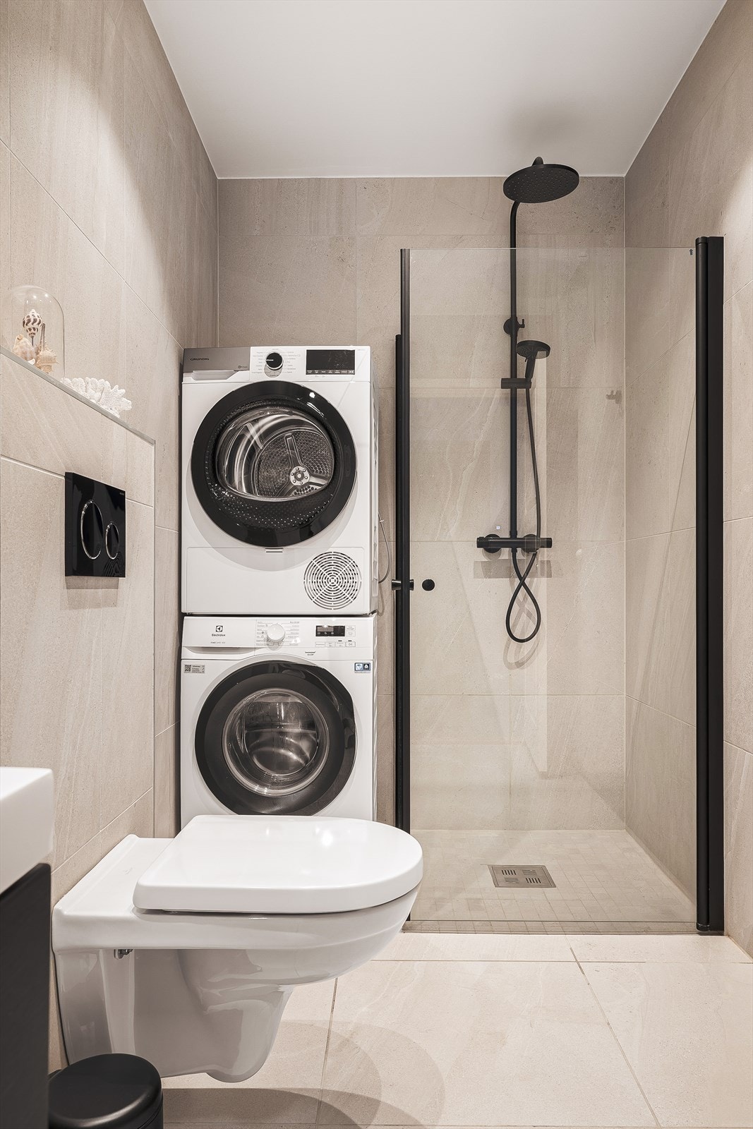 Badet er praktisk innredet med opplegg for vaskemaskin og plass til tørketrommel. Sorte detaljer gir rommet et stilrent preg. Galleribilde
