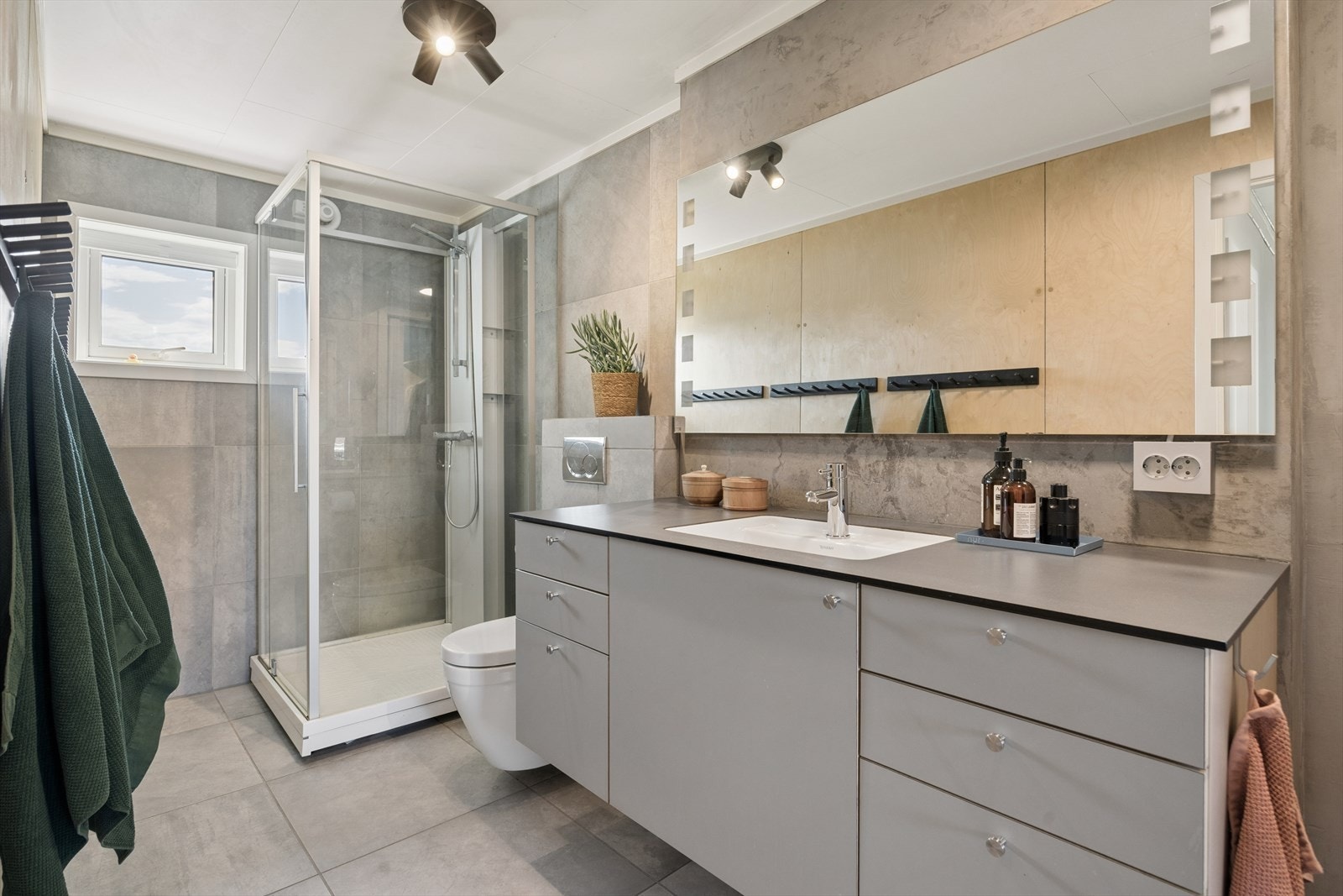 Badet er utstyrt med en romslig servantinnredning, veggmontert toalett med innebygd sisterne og et dusjkabinett. Galleribilde