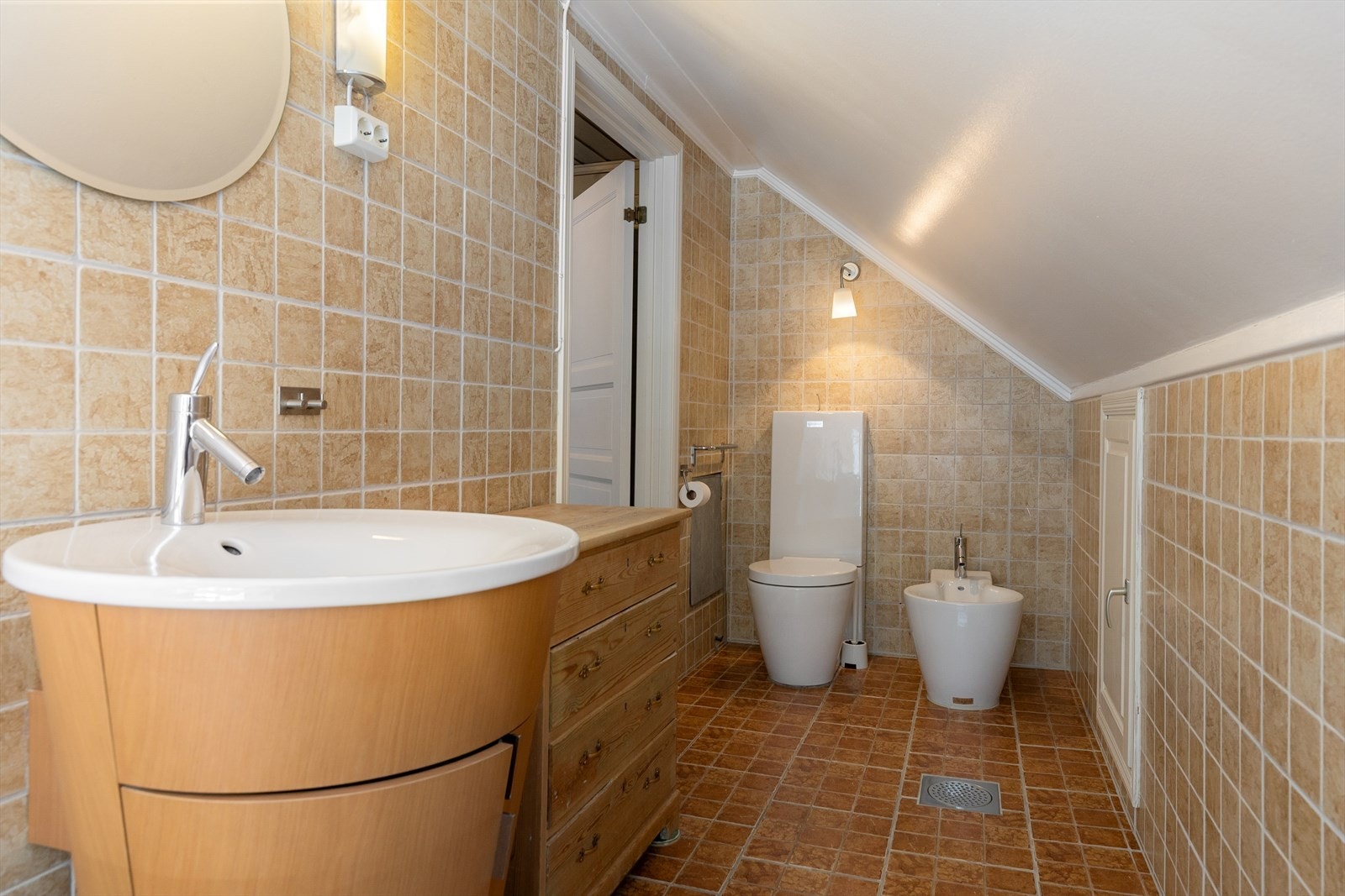 Badet er innredet med vegghengt toalett, rundt servant i finért skap, bidé, badekar og opplegg for vaskemaskin. Galleribilde