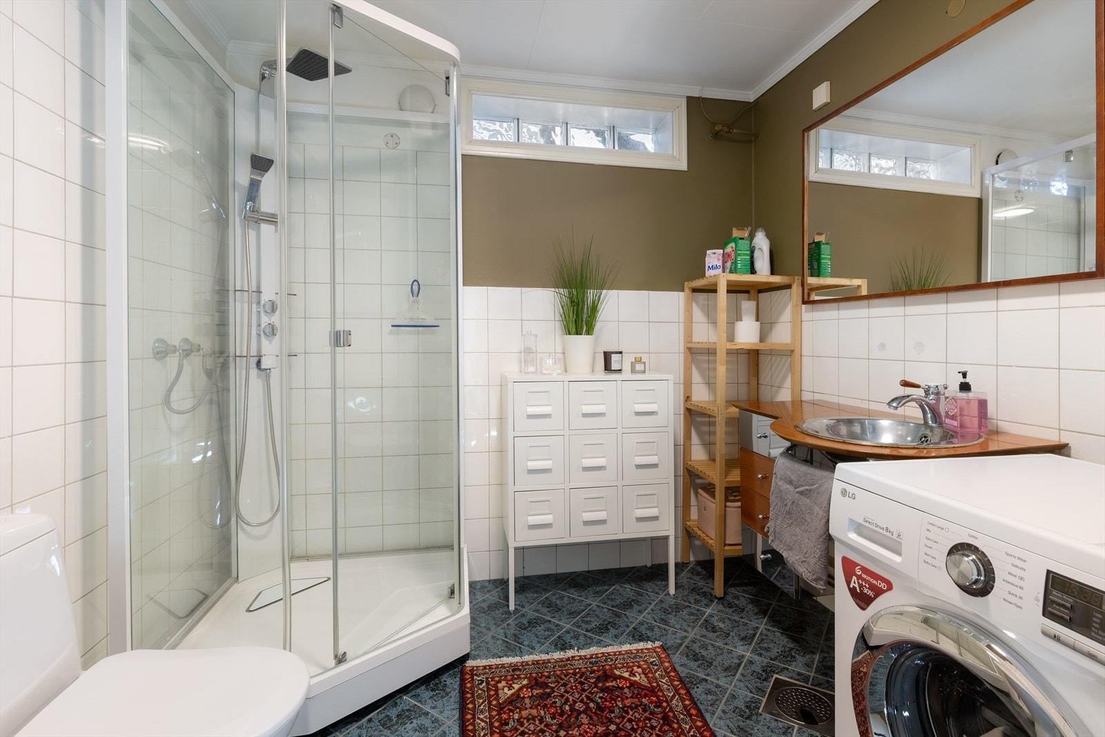 Lyst og praktisk bad/vaskerom med et tidløst uttrykk. Badet er utstyrt med dusjkabinett, toalett, servant i innredning, samt opplegg for vaskemaskin. Galleribilde