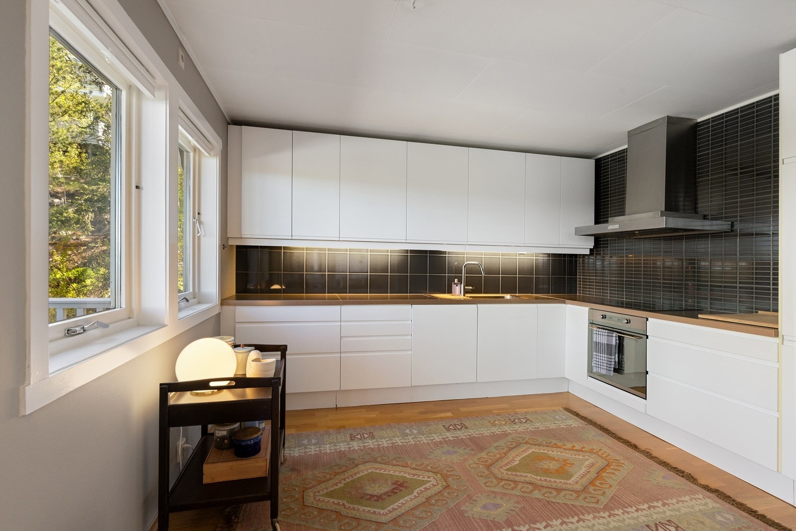 Delikat og tidløs kjøkkeninnredning med glatte hvite fronter- og integrerte gripehåndtak, laminat benkeplate med nedfelt stålkum med rillebrett. Galleribilde