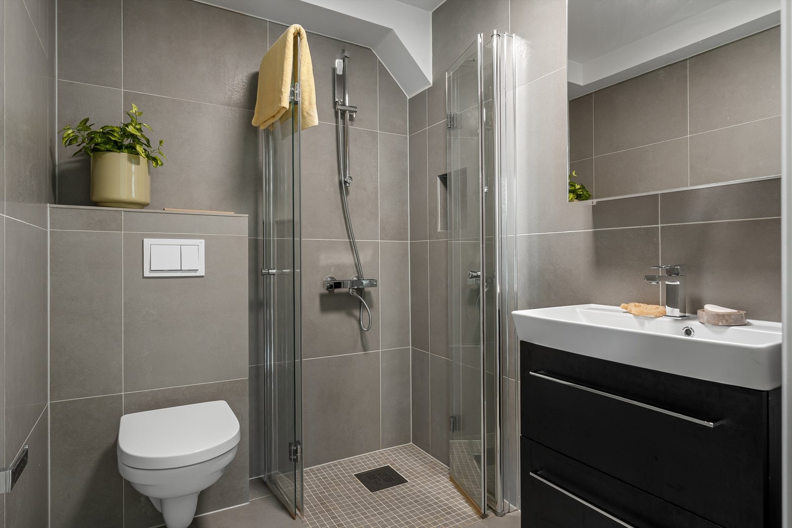 Badet i hovedetasjen er innredet med servant m/møblement, speil, vegghengt toalett og dusjhjørne med innfellbare dusjvegger. Galleribilde