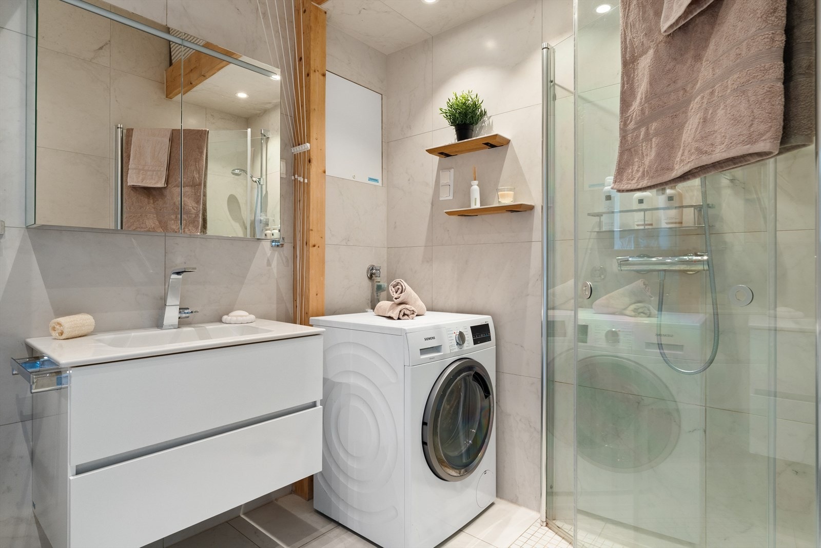 Badet har flotte, flislagte overflater og er utstyrt med elektrisk vifte på vegg og varmekabler i gulv. Badet er innredet med dusj med innfellbare dører i herdet glass, vegghengt toalett, opplegg for vaskemaskin og servantinnredning. Galleribilde