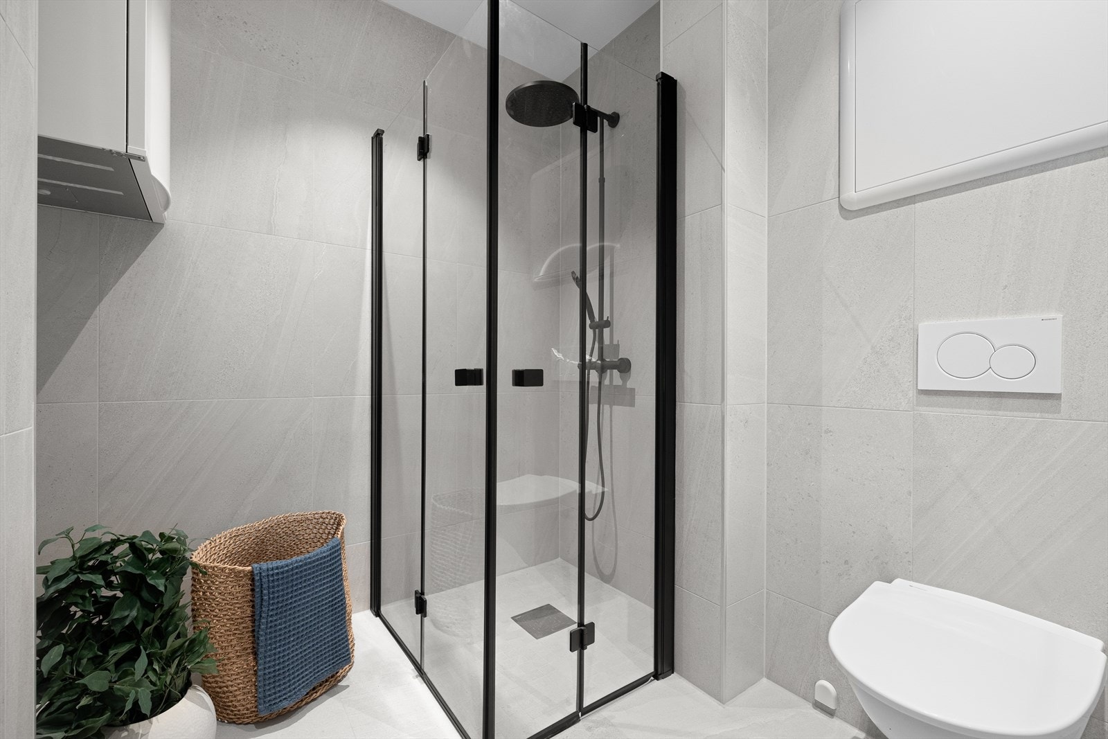 Badet inneholder vegghengt toalett, helstøpt servant med skuffer under, dusjdører i klart glass og opplegg for vaskemaskin. Galleribilde