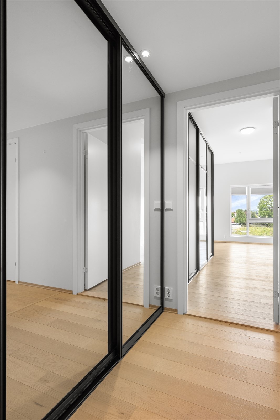 Entreen har en praktisk skyvedørsgarderobe med svarte rammer og speilflater som gir rommet karakter og praktisk oppbevaringsplass for yttertøy. Galleribilde
