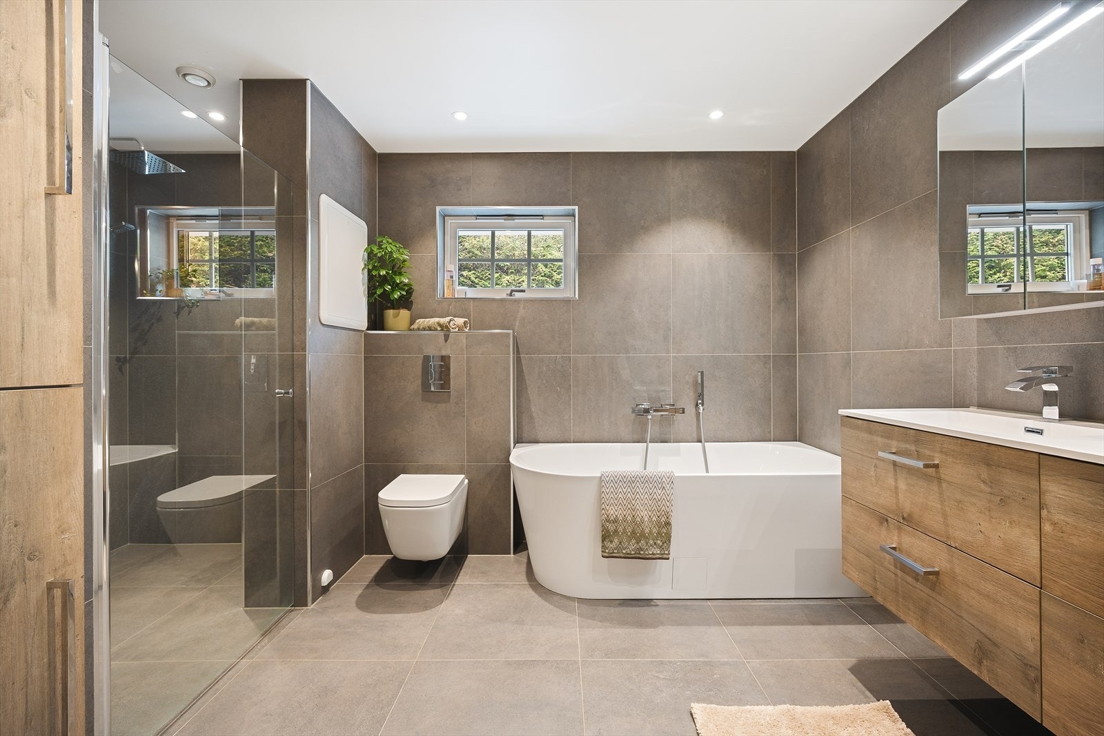 Badet er moderne og innbydende, med en smakfull dobbel dusjløsning, og er innredet med doble servanter, veggmontert toalett, badekar samt dusjhjørne med to tak- og hånddusjer, noe som gir en gjennomgående god komfort og et eksklusivt preg. Galleribilde