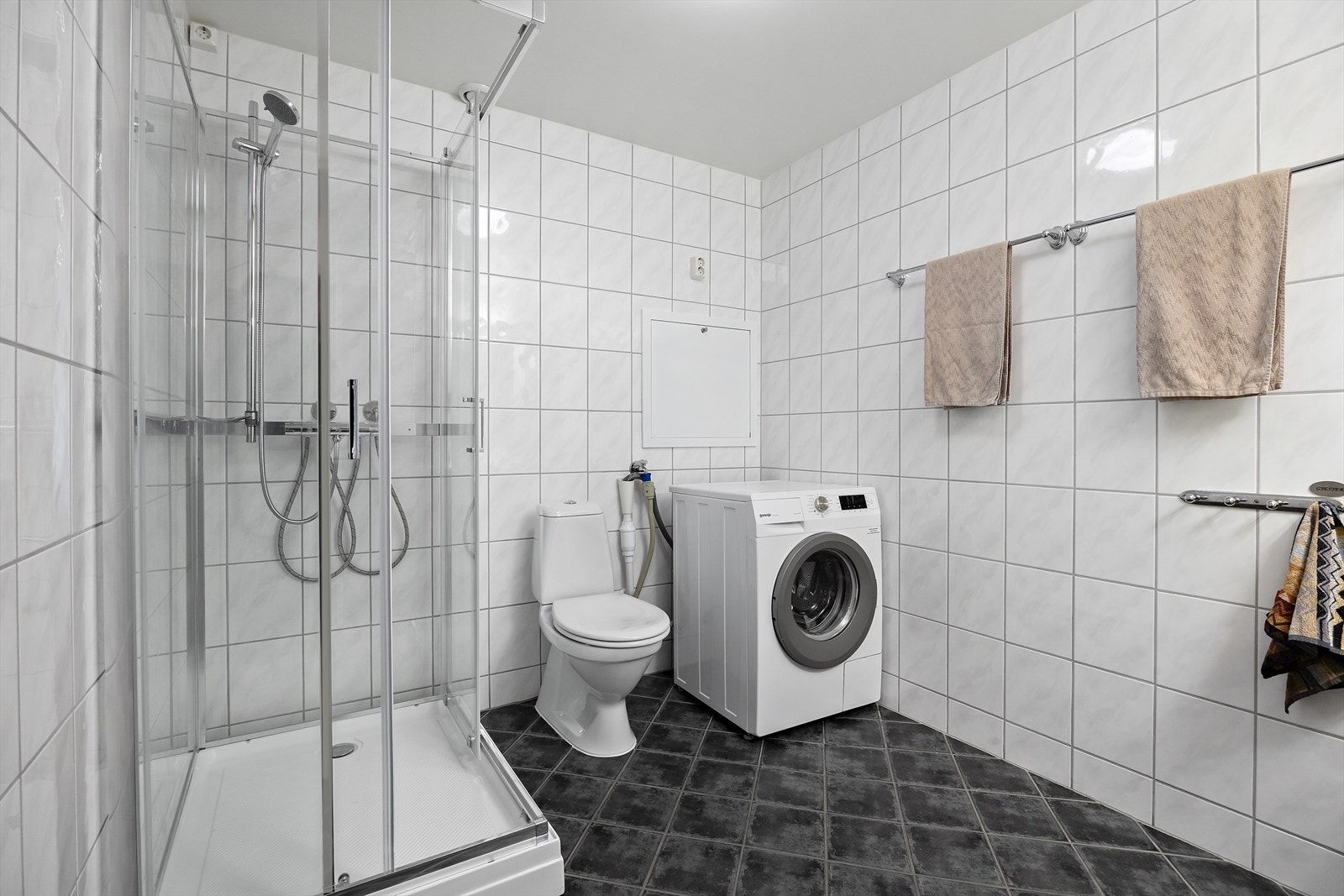 Romslig, helfliset bad med elektrisk gulvvarme. Badet inneholder nyere dusjkabinett, toalett og opplegg for vaskemaskin. Galleribilde