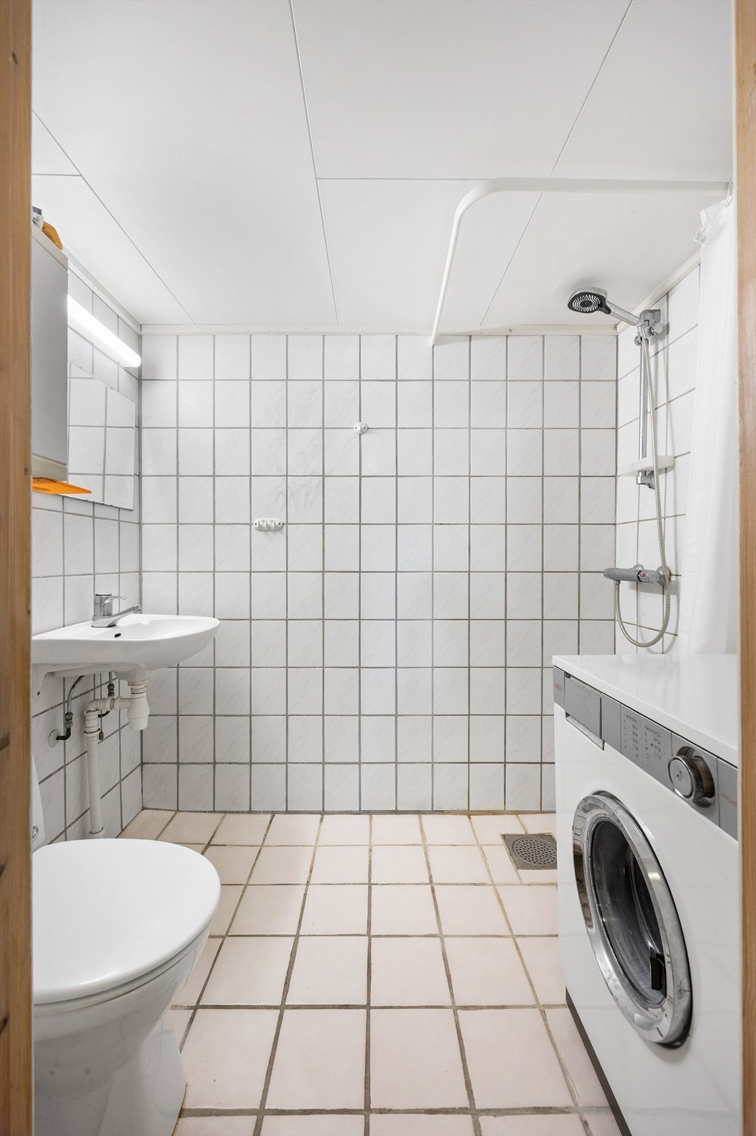 Badet i kjelleren er fra ca. 1990, med flislagte overflater, dusjløsning og opplegg for vaskemaskin. Galleribilde