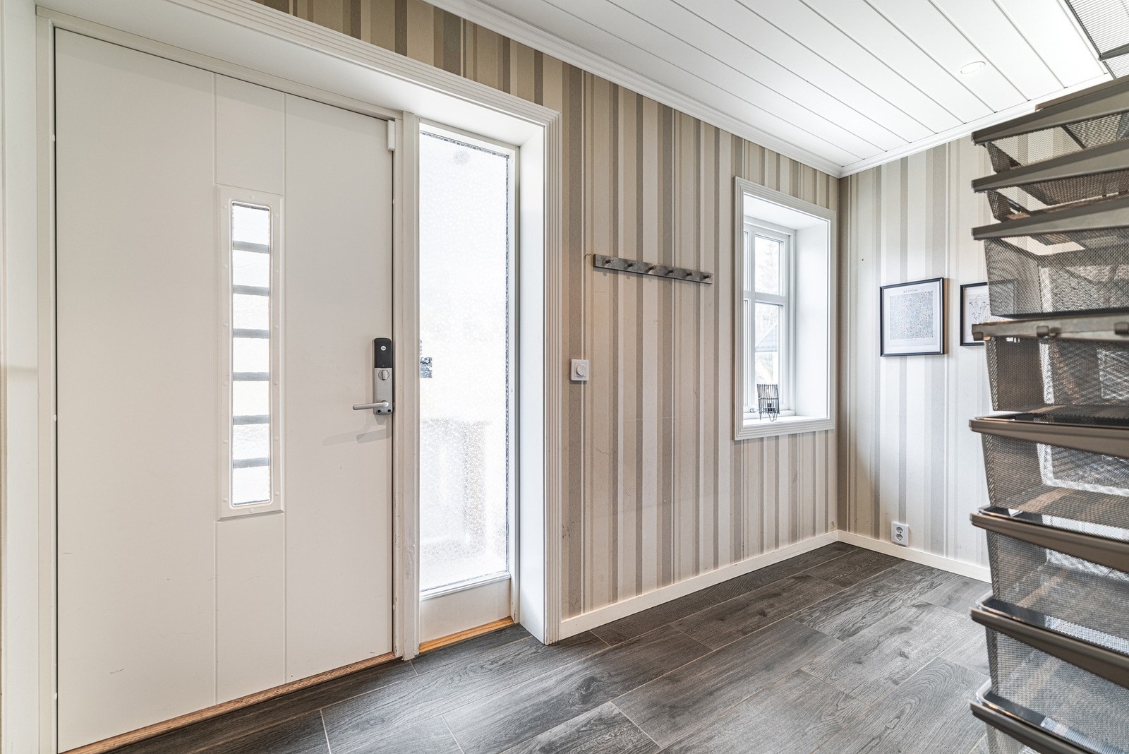 Romslig entré med ytterdør med glassfelt, knagger og oppbevaringssystem til klær. Galleribilde