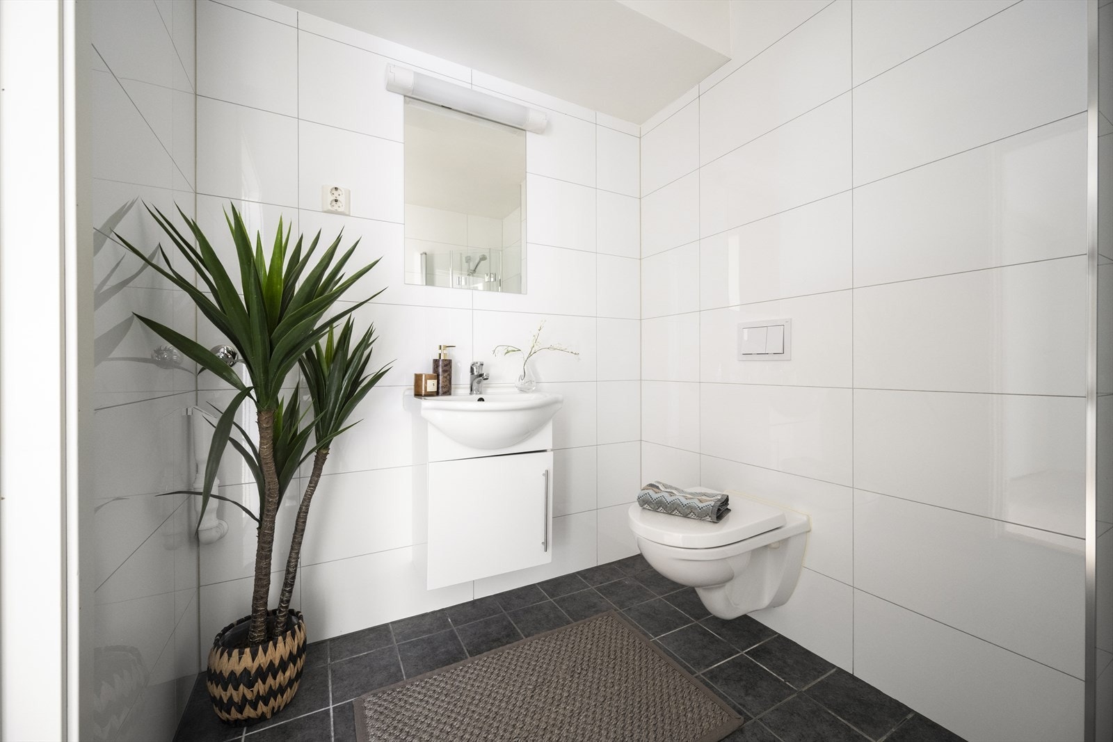 Innredning og garnityr på badet består av dusjhjørne med innfellbare glassdører og blandebatteri, vegghengt toalett og baderomsinnredning med skap, heldekkende servant og ettgreps blandebatteri, speil og belysning på vegg. Galleribilde