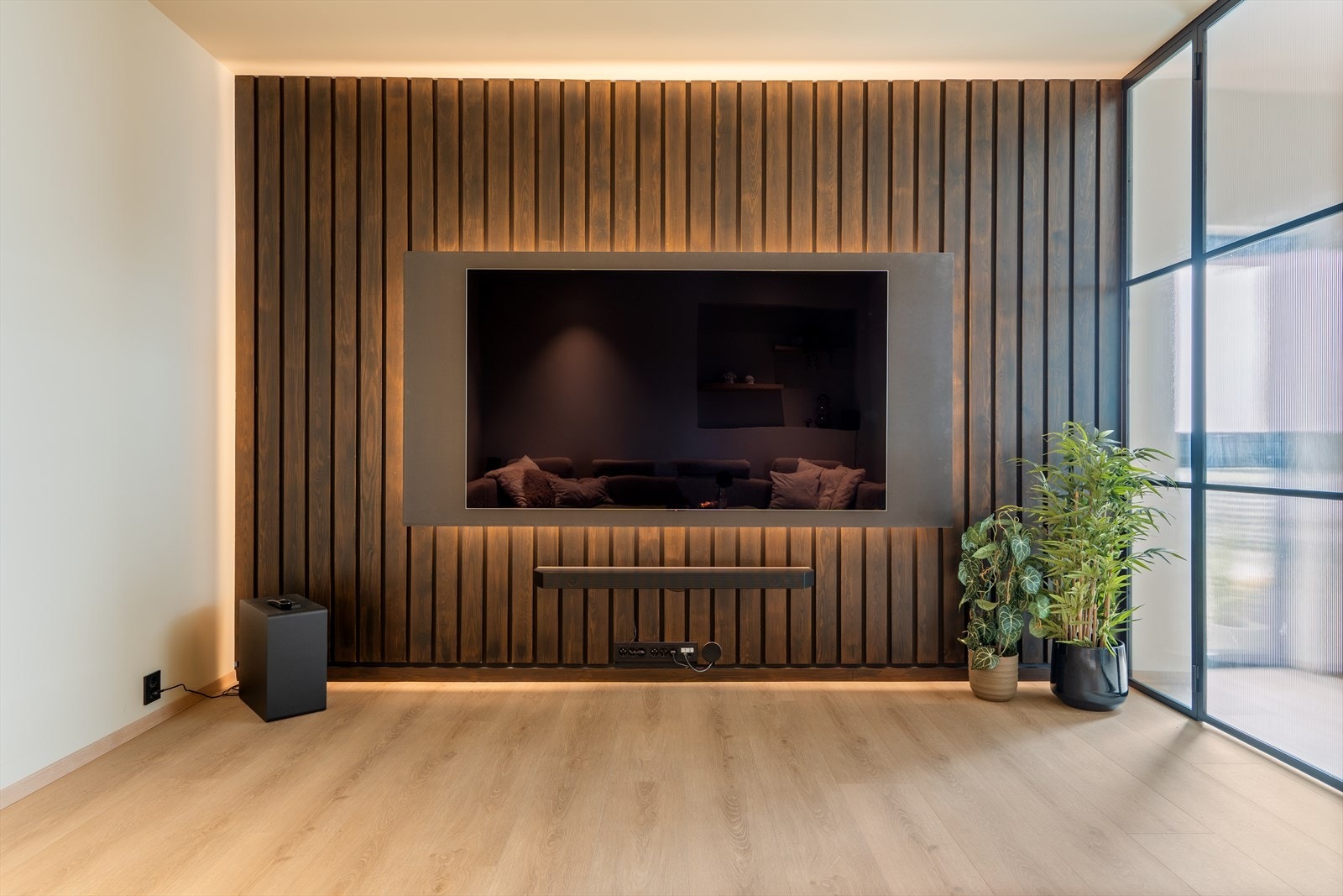 Rommet fremstår lyst og moderne, med en stilfull spilevegg som danner en flott ramme rundt den vegghengte TV-en. Galleribilde