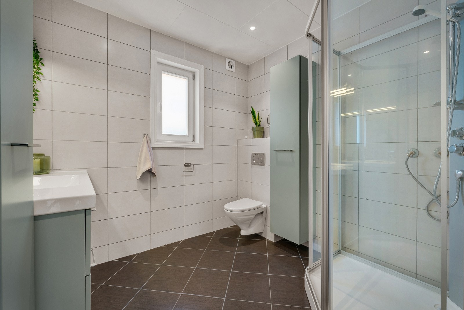 Badet fremstår som funksjonelt med flislagte overflater, varmekabler i gulv og nytt dusjkabinett installert i 2025. Galleribilde