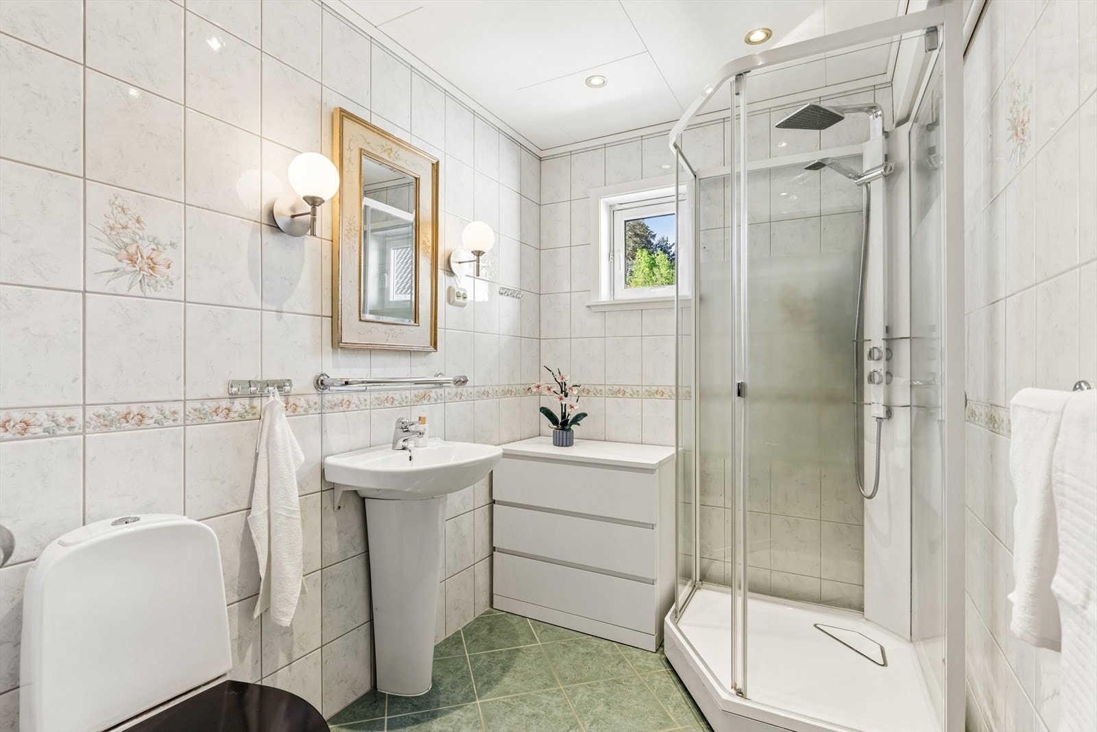Badet er fra byggetiden og har fliser på vegger. Dusjkabinett må brukes i rommet. Innredning og sanitærutstyr er ok vedlikeholdt. Det er boligventilasjon med avtrekksventil. Galleribilde