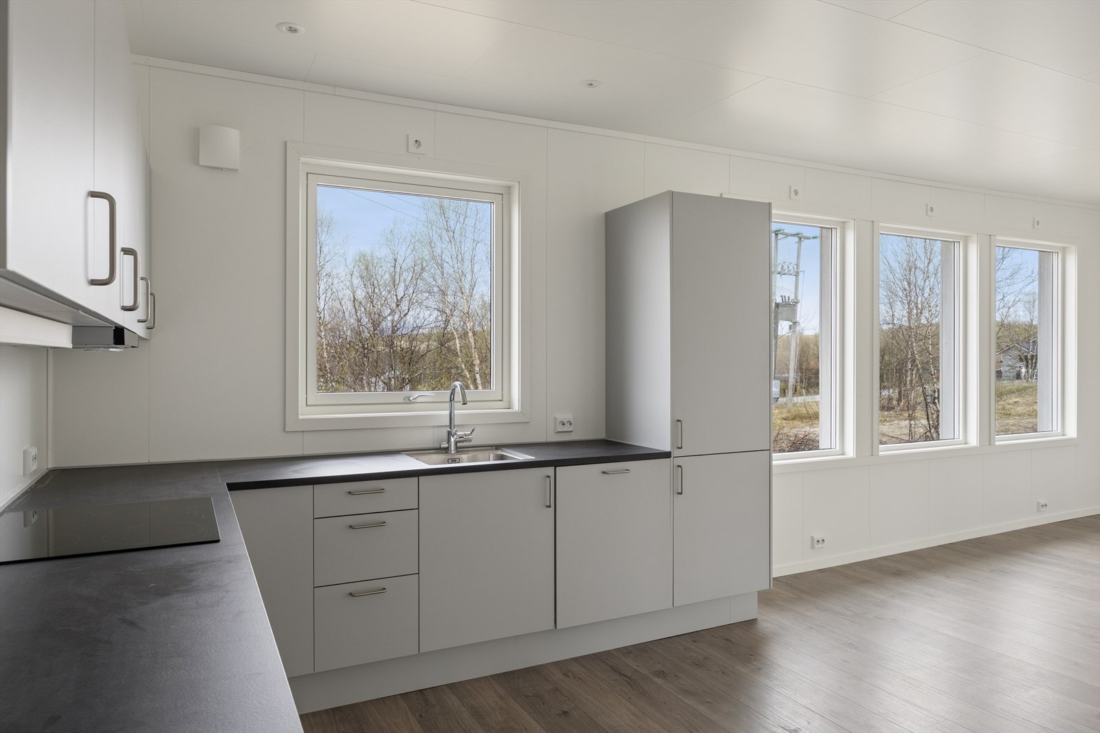 Kjøkkeninnredning med slette, grå fronter og laminat benkeplate. Det er avsatt plass til kjøleskap. Galleribilde
