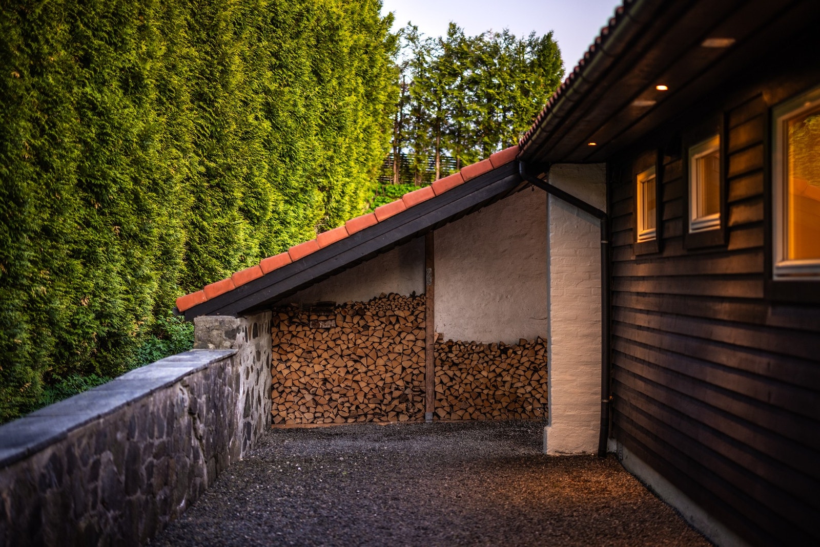 På baksiden av huset er det lagt godt til rette for vedlagring, med en overbygget og skjermet løsning som holder veden ryddig og lett tilgjengelig. Galleribilde