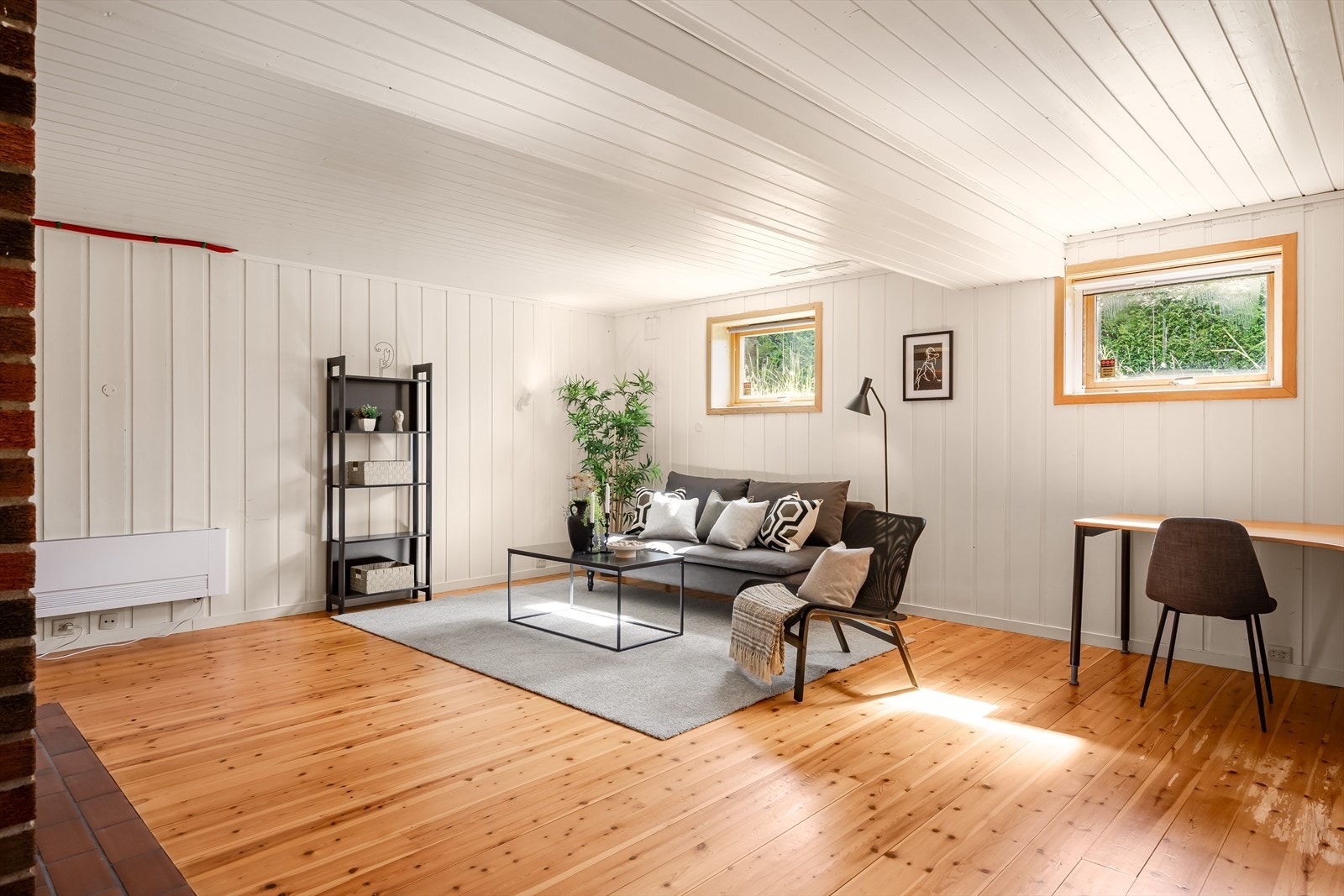 Stor, lys og hyggelig kjellerstue med lakkerte tregulv og lysmalt panel på veggene. Galleribilde