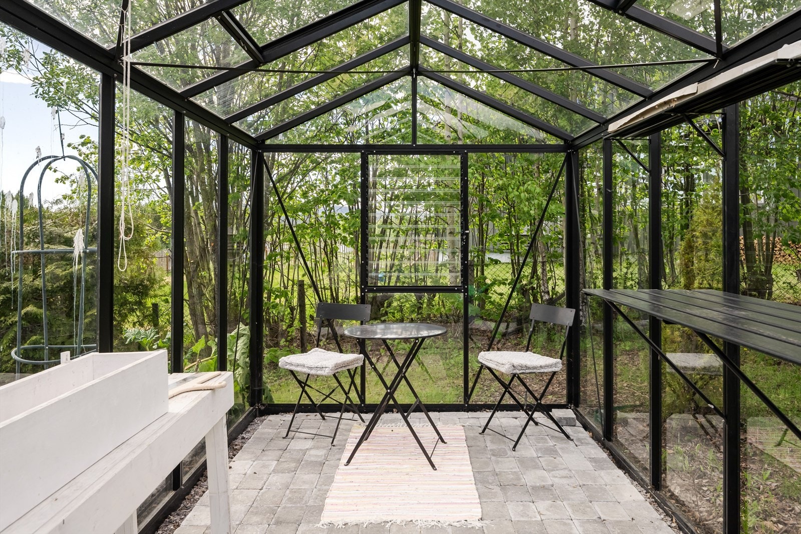 Flott drivhus på 10m² med belegningsstein på gulv og sorte metallskinner med glassfelt. Galleribilde