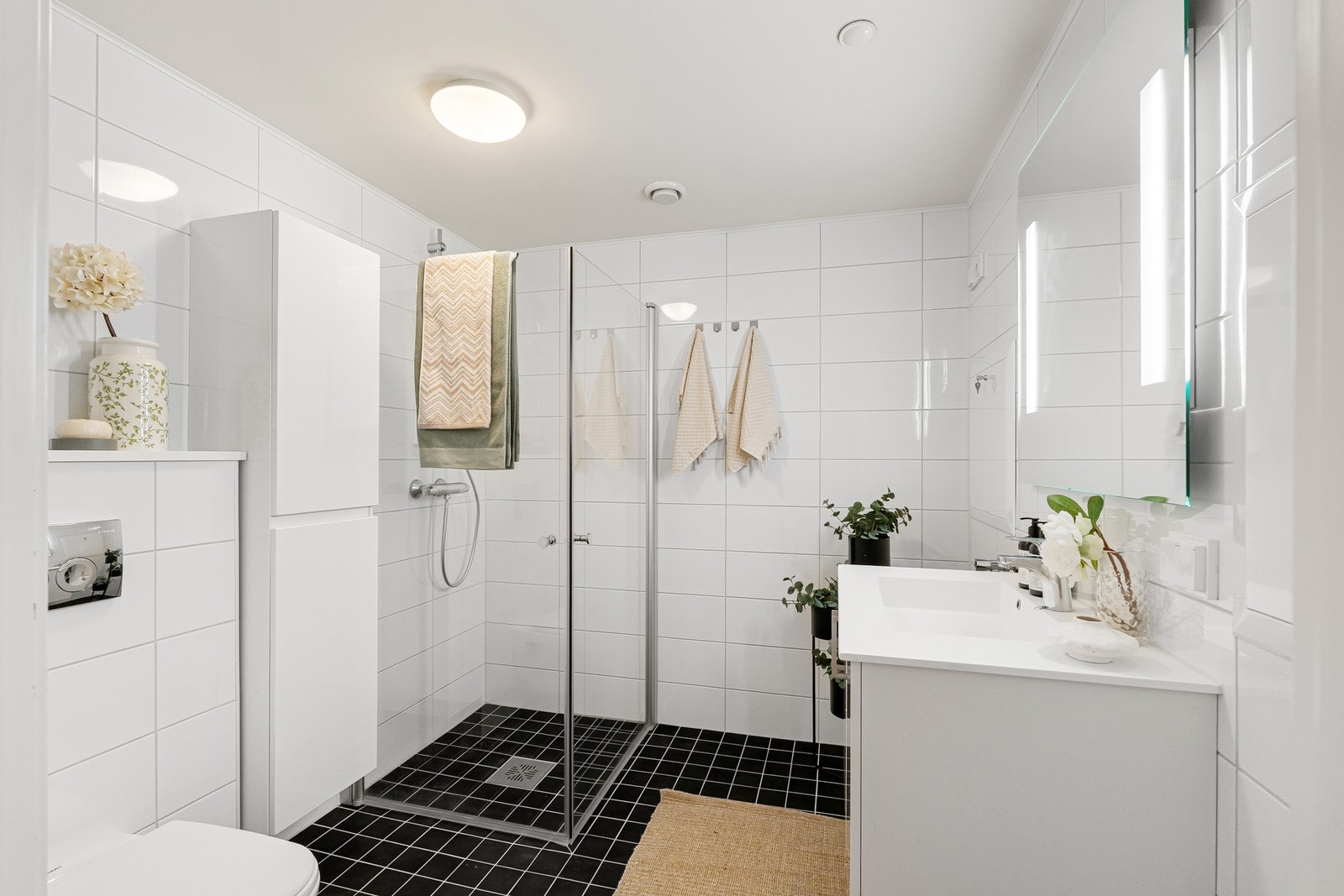 Badet måler 4,9 kvm og er innredet med dusj med innfellbare dører i glass, veggmontert WC, kran og avløp for vaskemaskin, servant med underskap og speil. Galleribilde