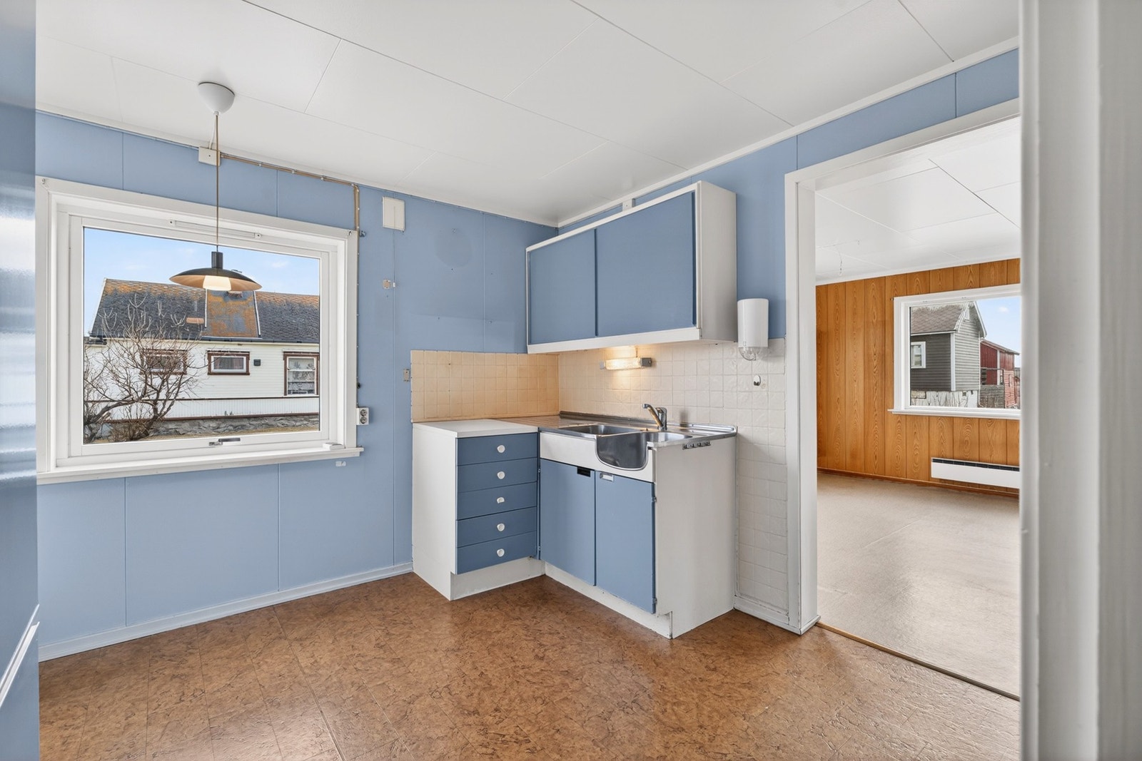 Kjøkken med eldre innredning, utstyrt med benkebeslag i stål og laminat benkeplate. Galleribilde