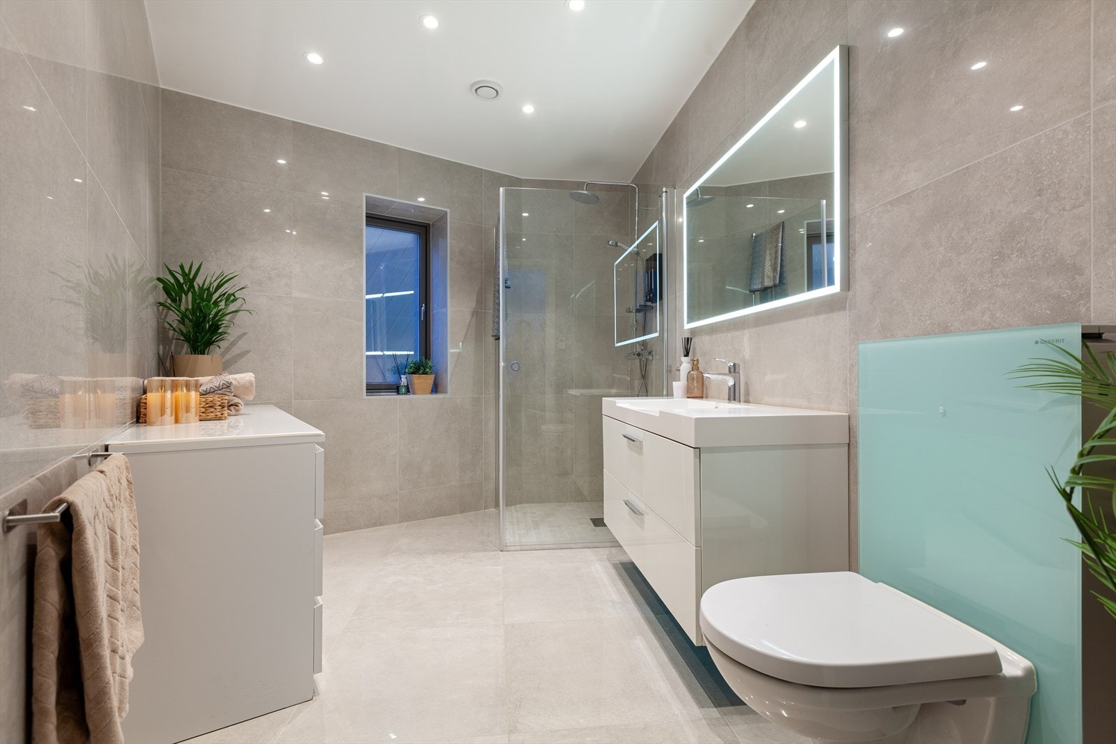 Ett av boligens to store bad. Badet er i delikat utførelse med lyse fliser (60*60 cm ) med vannbåren varme i gulv. Innfelte downlights i tak og ramme speillys. Galleribilde