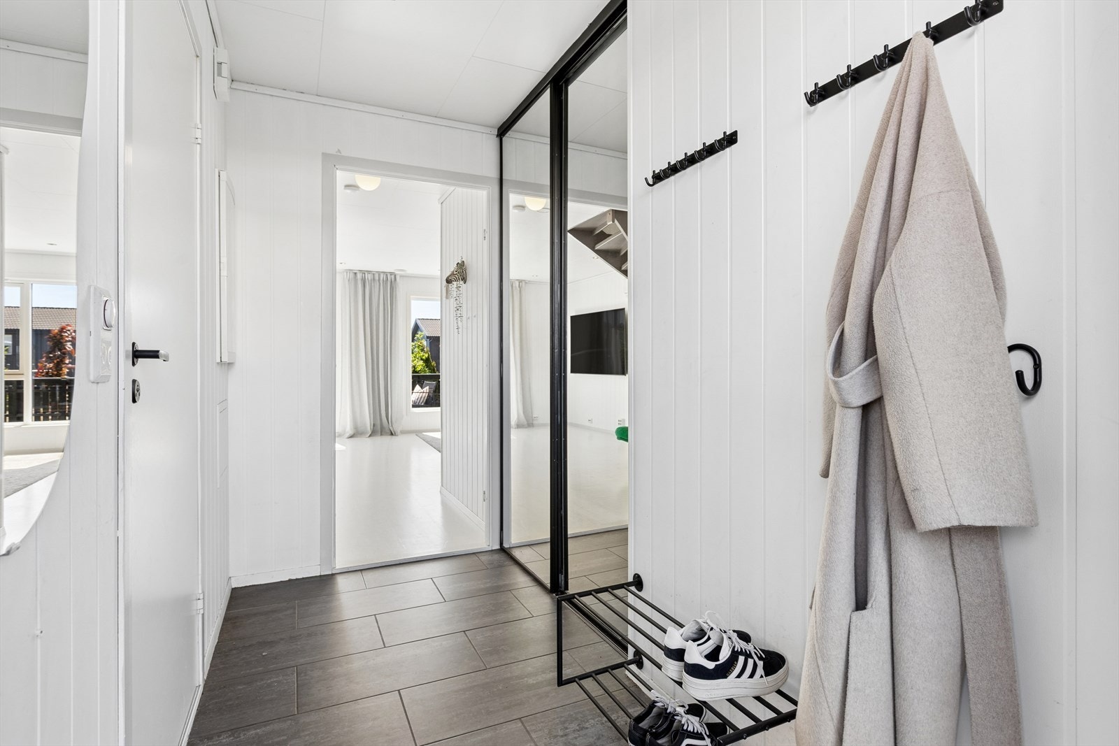Entreen er innredet med fliselagt gulv og hvite panelvegger. Integrert skyvedørsgarderobe. God plass til å henge fra seg ytterklær. Galleribilde