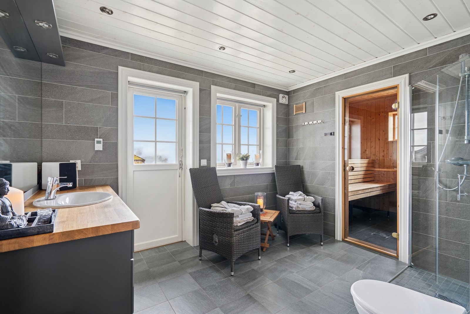 Badet i første etasje er romslig og moderne, med flislagte gulv og vegger, veggmontert toalett og dusjnisje med glassdør. Innredningen er stilren og funksjonell, og rommet har direkte adkomst til uteområdet - perfekt etter en tur i badstuen. Galleribilde