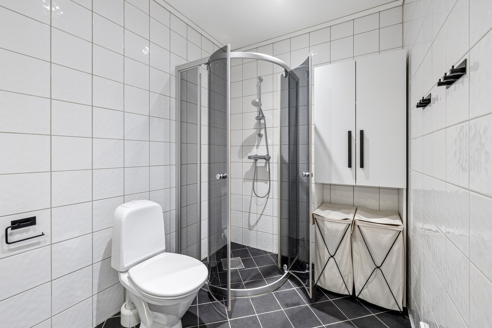 Badet er utstyrt med dusjvegger, gulvmontert toalett og servant med underskap. Galleribilde