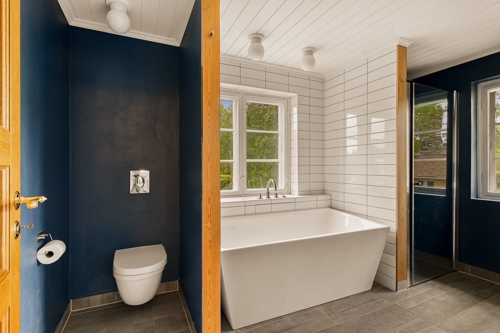 Badet har flislagt gulv, vegghengt toalett og malt trepanel i taket. Galleribilde