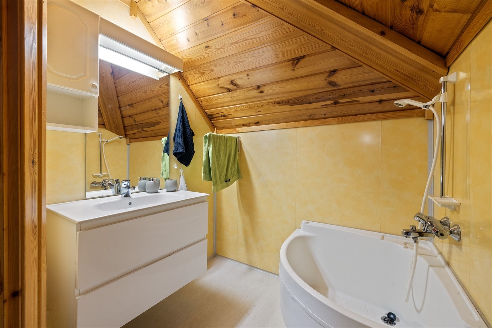 Badet har belegg på gulv og våtromsplater på vegger. Baderommet er utstyrt med servant over skuffeinnredning, speil med overliggende belysning, badekar og toalett Galleribilde