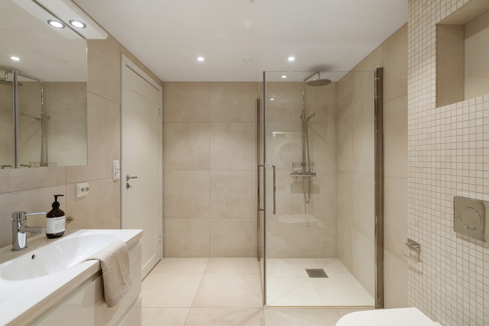 Badet inneholder dusjhjørne med innfellbare glassdører, vegghengt toalett og servantinnredning. Galleribilde