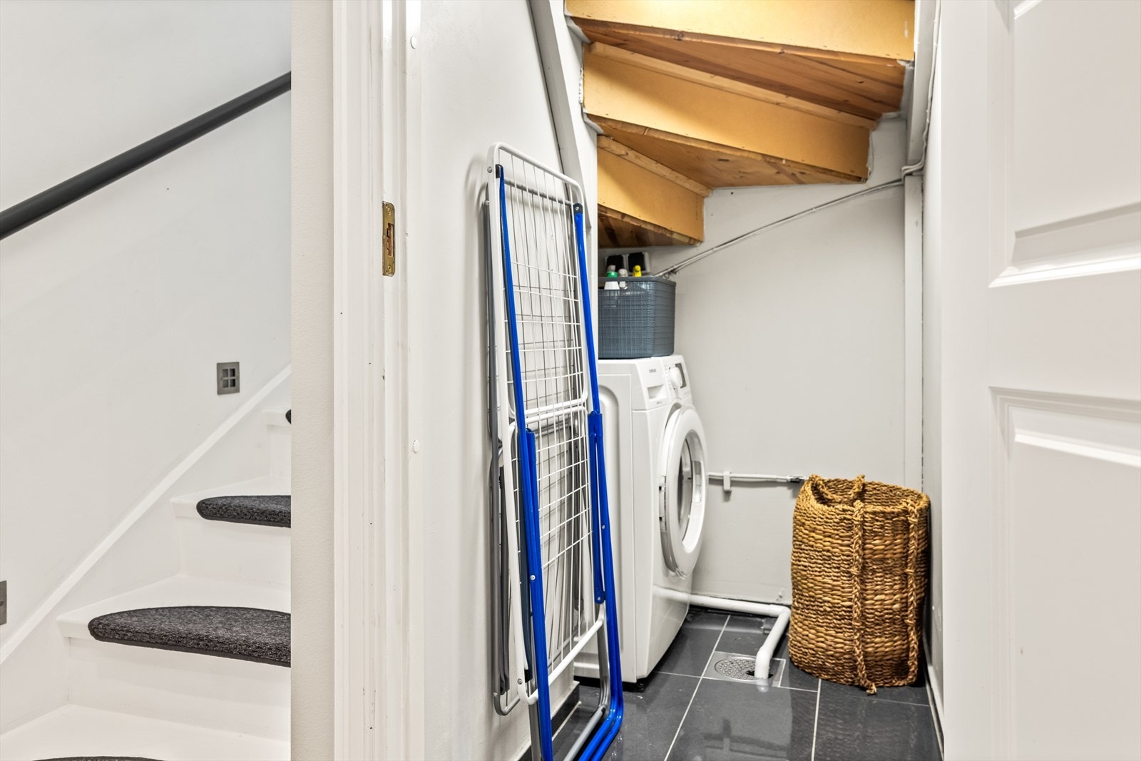 Kott/vaskerom under trappen med fliser på gulvet, sluk og opplegg for vaskemaskin. Galleribilde