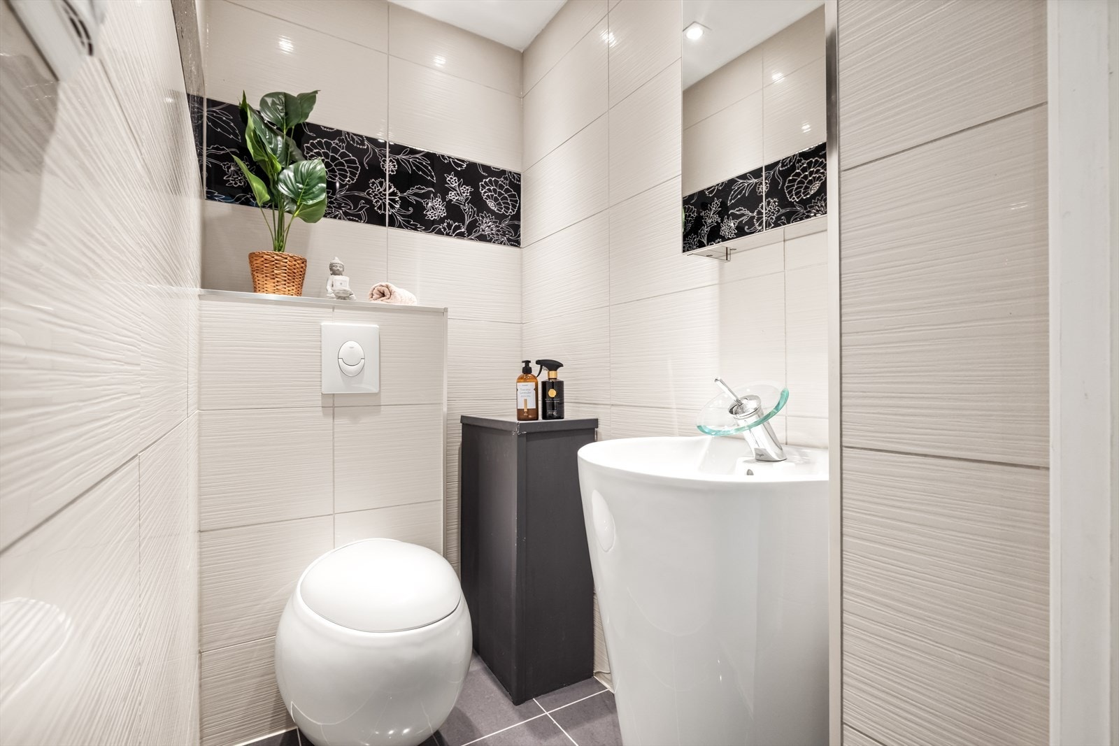 Toalettrommet har flislagte overflater, downlightsbelysning og innredning med vegghengt toalett og servant med speilskap over. Galleribilde