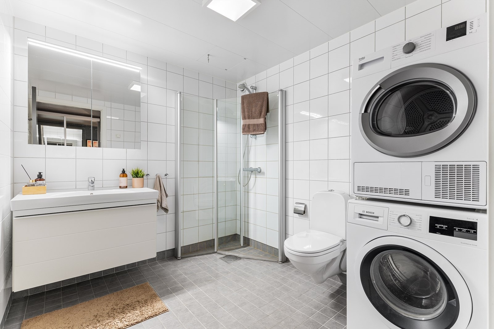 Flislagt baderom med gulvvarme, dusjhjørne med glassdører, vegghengt toalett og opplegg for vaskemaskin. Mekanisk avtrekk sikrer godt inneklima. Badet er oppmålt til 5,5 m² Galleribilde