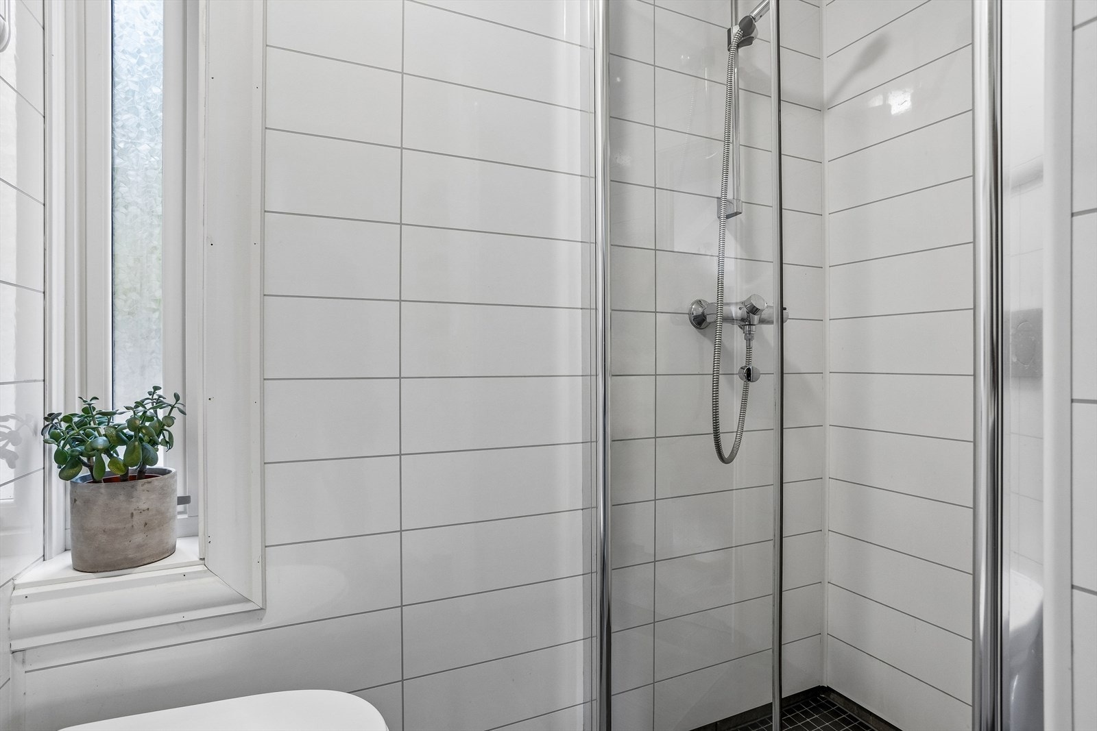 Flislagt gulv på badet. Dusjhjørnet har innfellbare dører i klart glass som frigjør gulvplass. Galleribilde