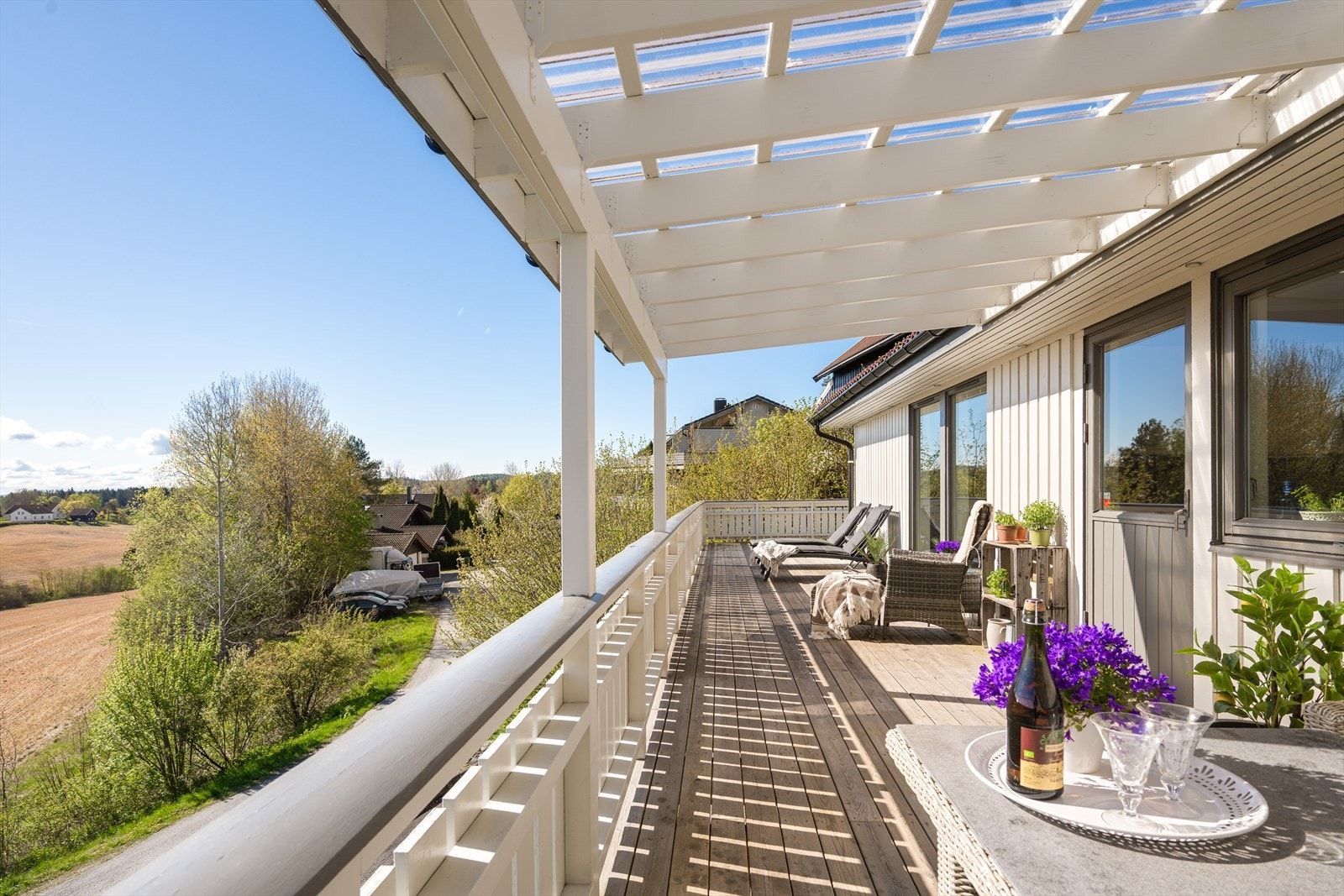 Den store verandaen fungerer som en naturlig forlengelse av boligens oppholdsrom og gir rikelig med plass til både spisegrupper, loungeområder og rolige solkroker. Pergolaen ved kjøkkenutgangen skaper en lun og stemningsfull ramme rundt uteplassen. Galleribilde