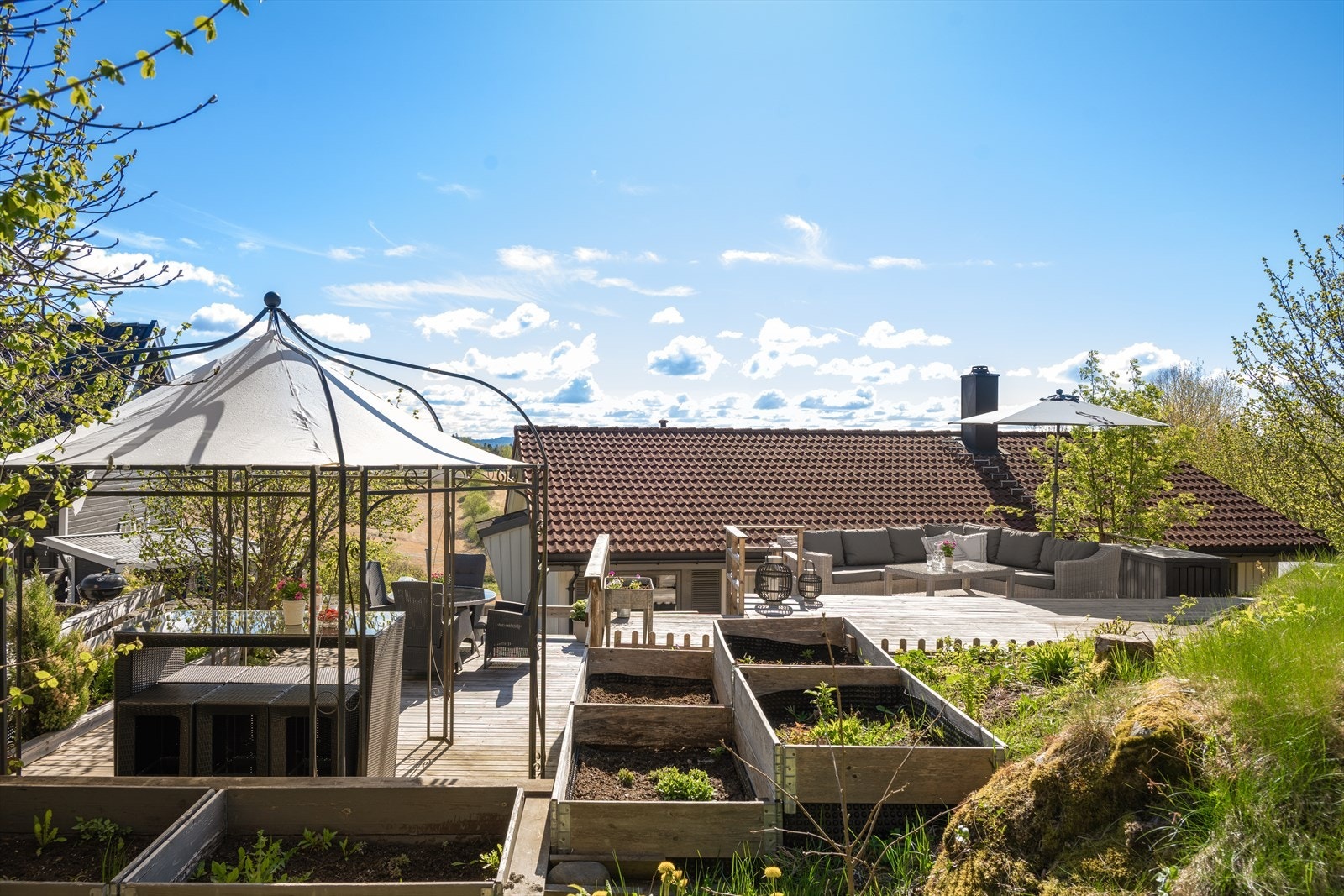 En skjermet og solrik uteoase hvor flere flotte terrasseplattinger sys sømløst og naturlig inn i det vakre terrenget. Her kan sommerdagene nytes i rolige omgivelser med god plass til både avslapning og hyggelige sammenkomster. Galleribilde