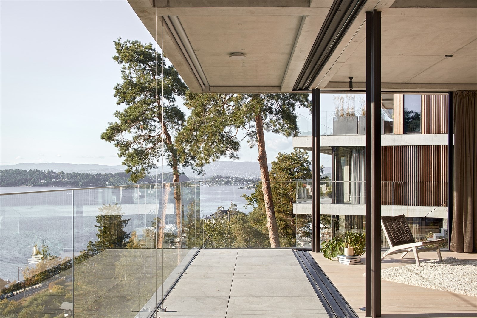Uteareal med glassrekkverk og utsyn mot fjorden, ett av flere utvendige oppholdsarealer tilknyttet boligen Galleribilde